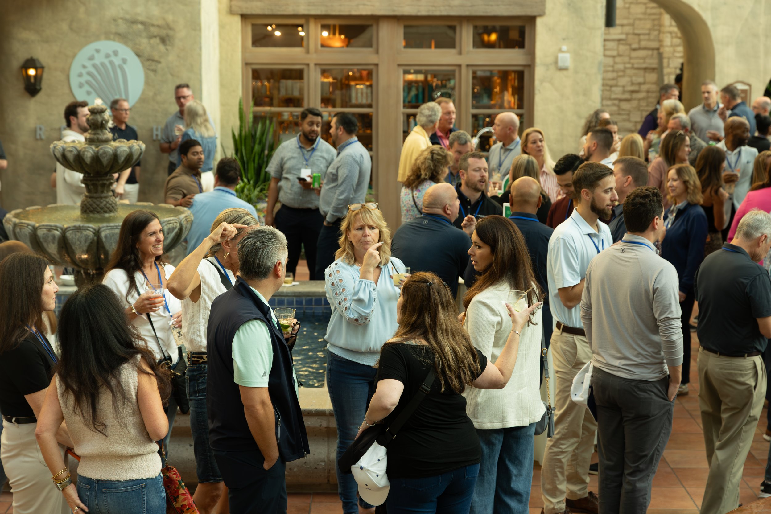 Crowded indoor networking event with people mingling around a decorative fountain and bar.