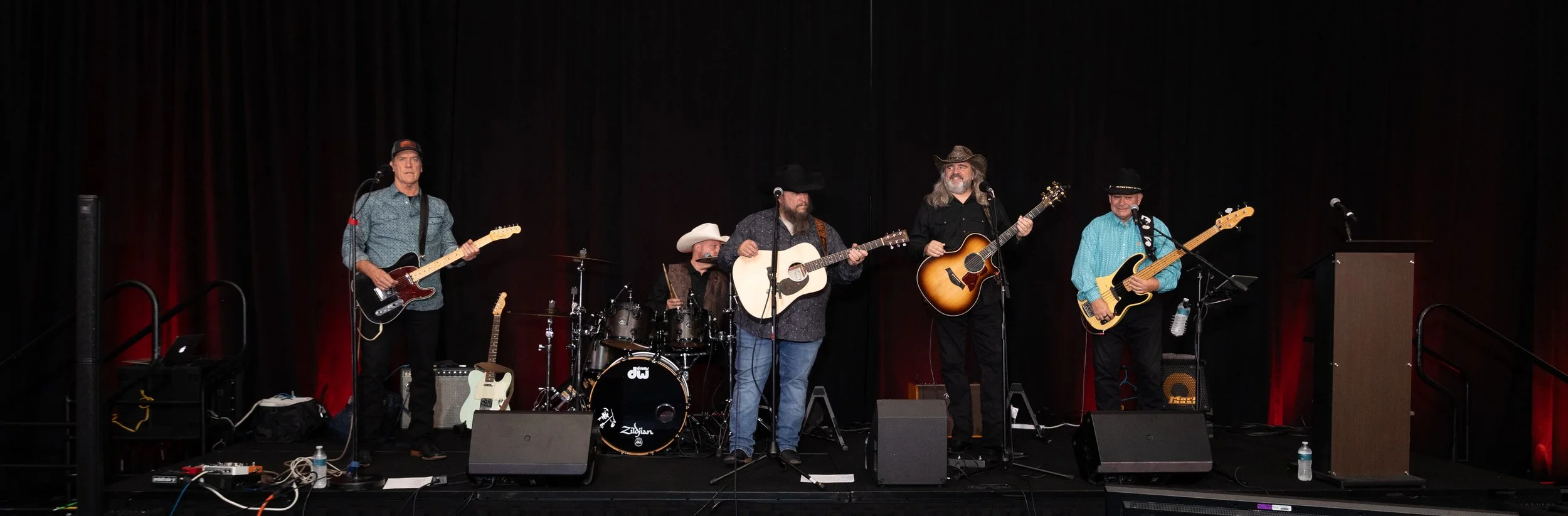 Country music band performing on stage with guitars, bass, drums, microphones, and amplifiers