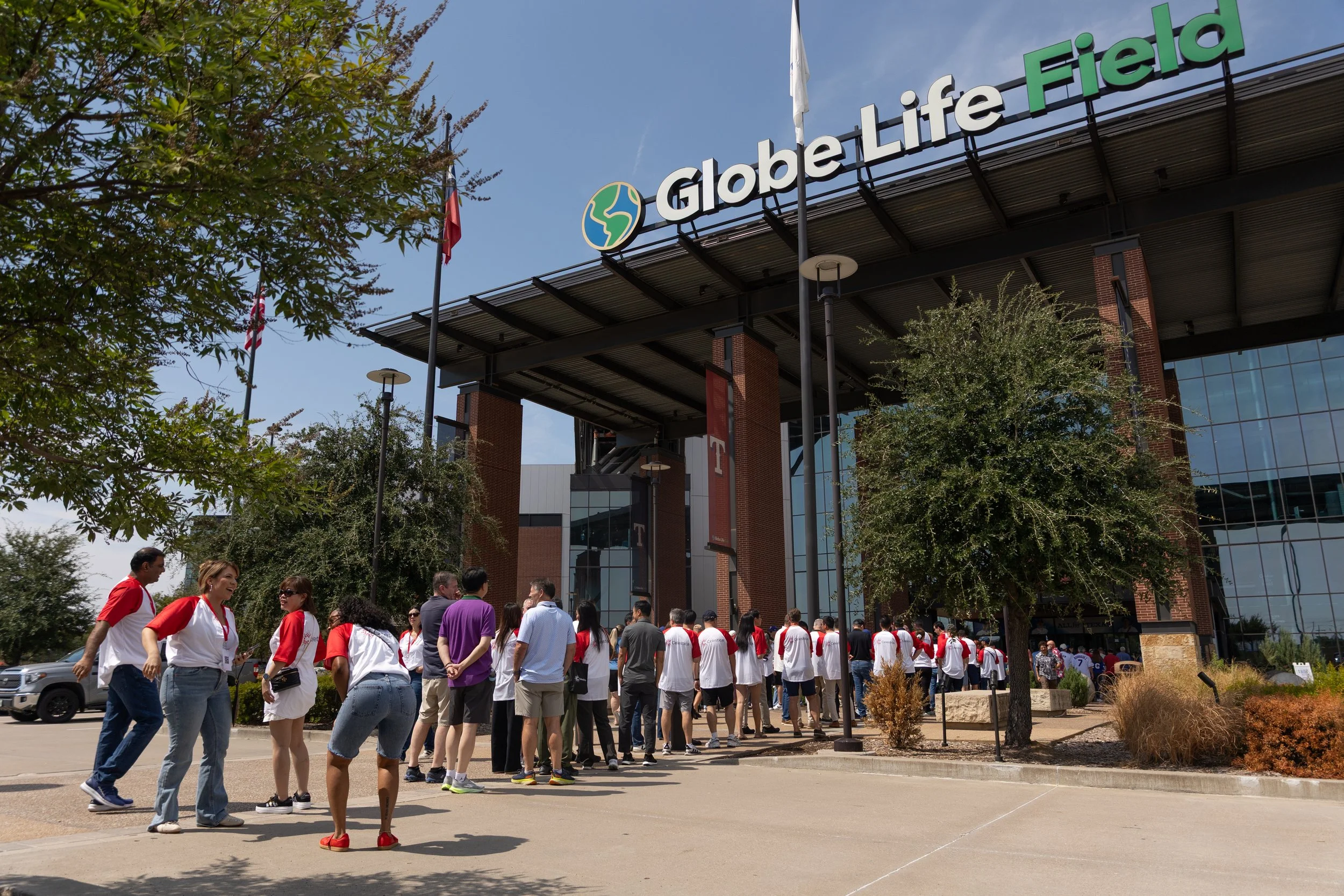 Crowd entering Globe Life Field stadium beneath its sign on a sunny day.