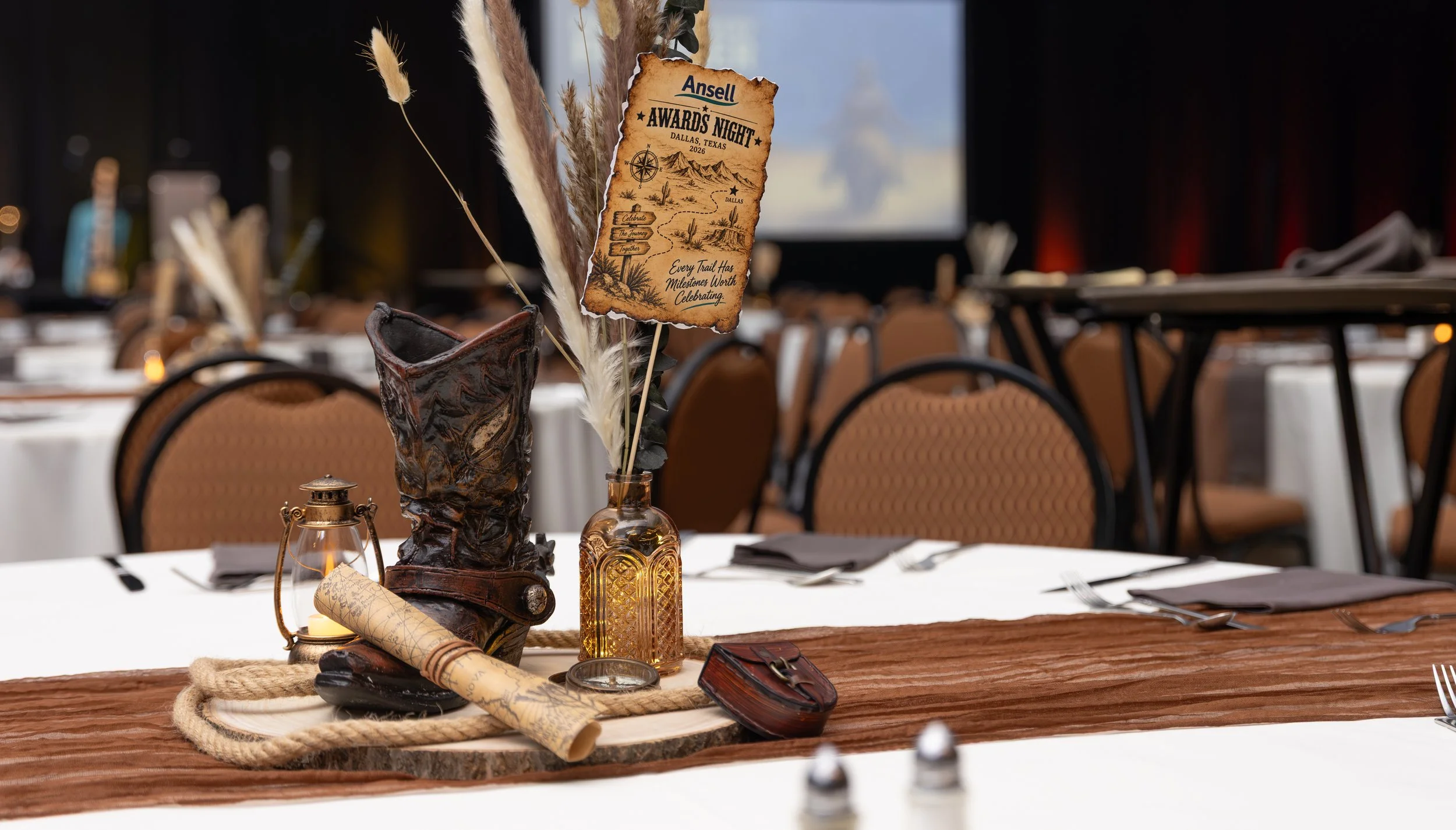 Western-themed banquet table centerpiece with dried grasses, rustic decor, lantern, leather boot, and engraved Ansell Awards Night sign in Dallas, Texas