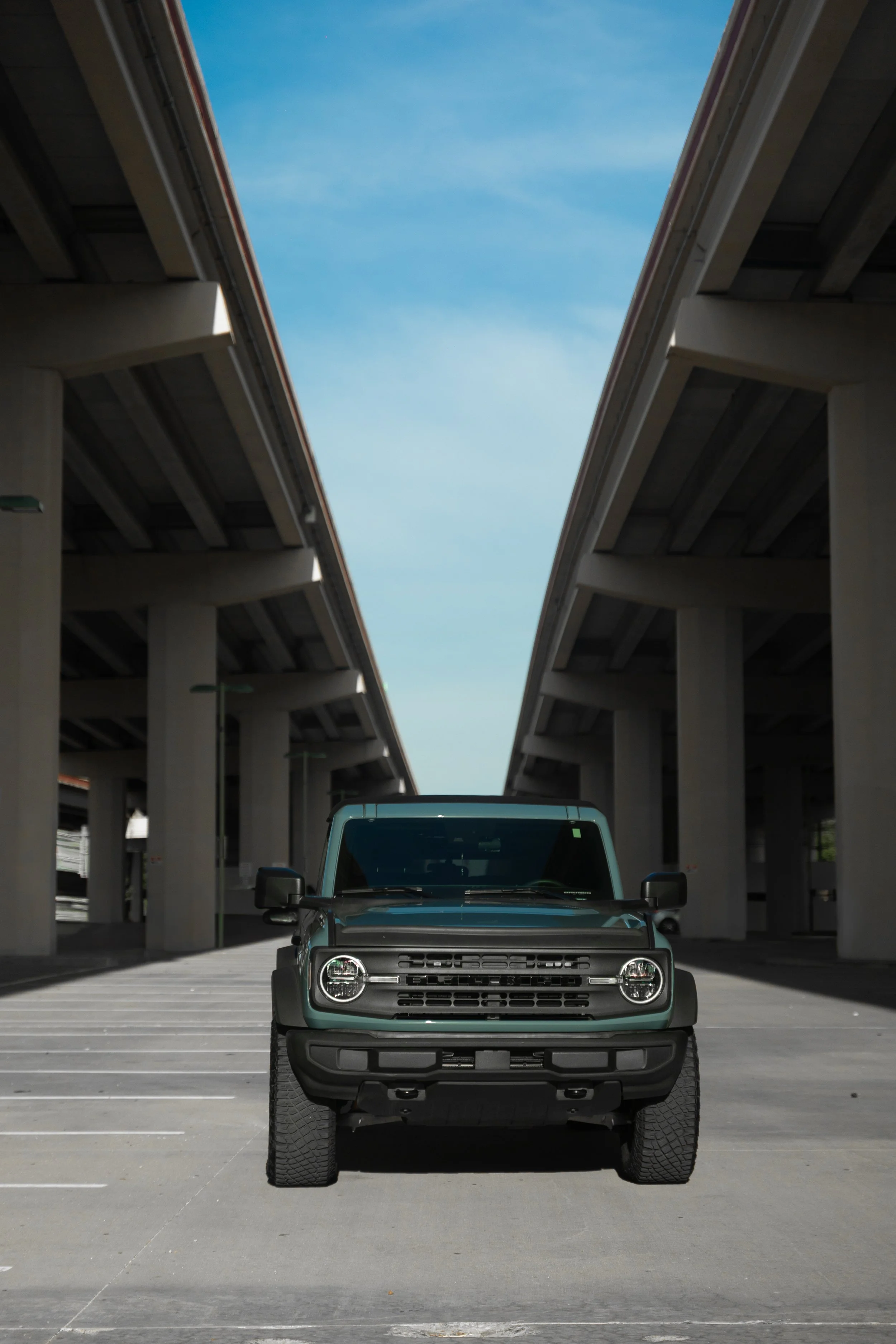 A black pickup truck parked in a parking lot under a large concrete bridge with the sky visible through the gap.