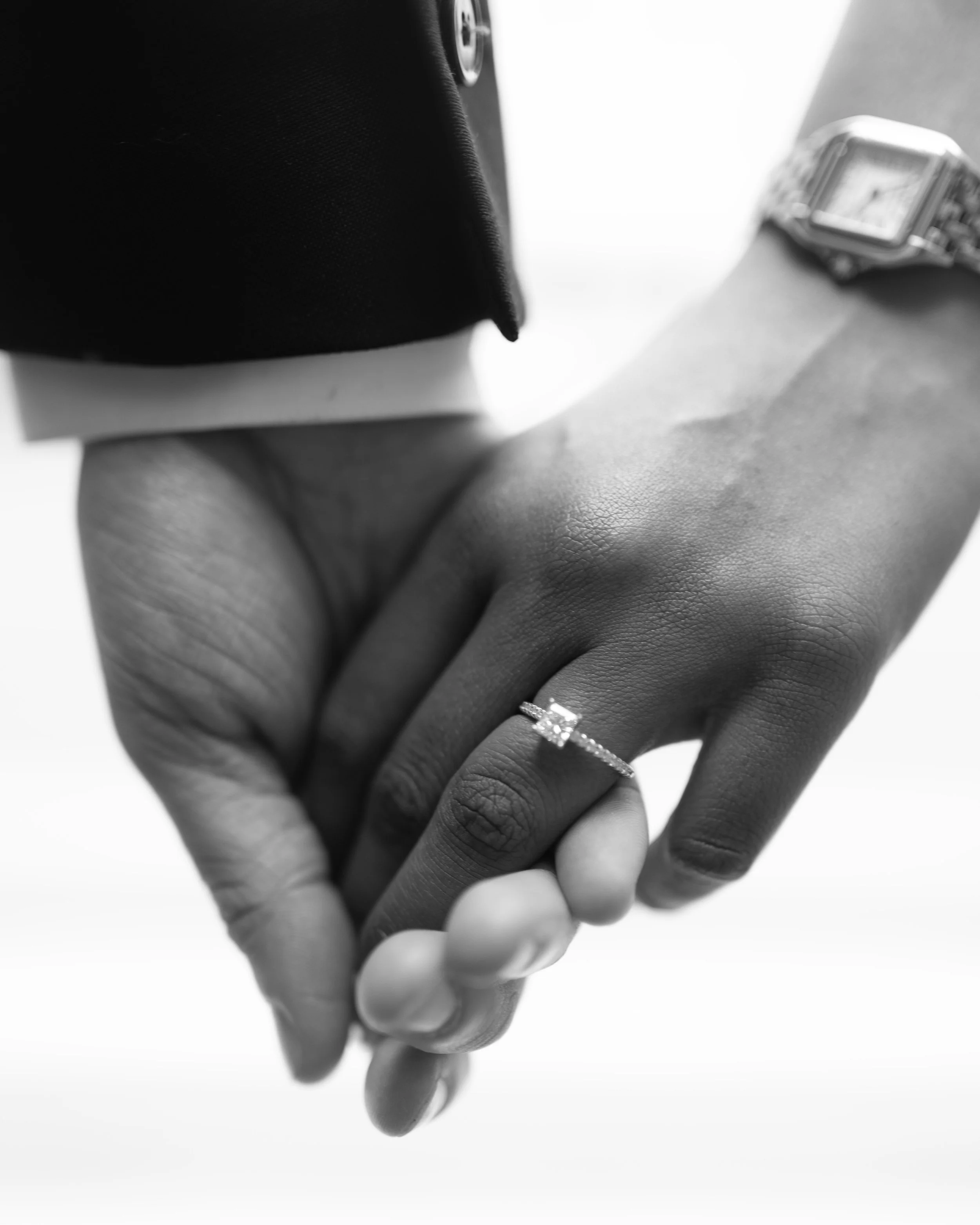 Close-up of two hands holding each other, one with a diamond ring and watch, black and white photo.