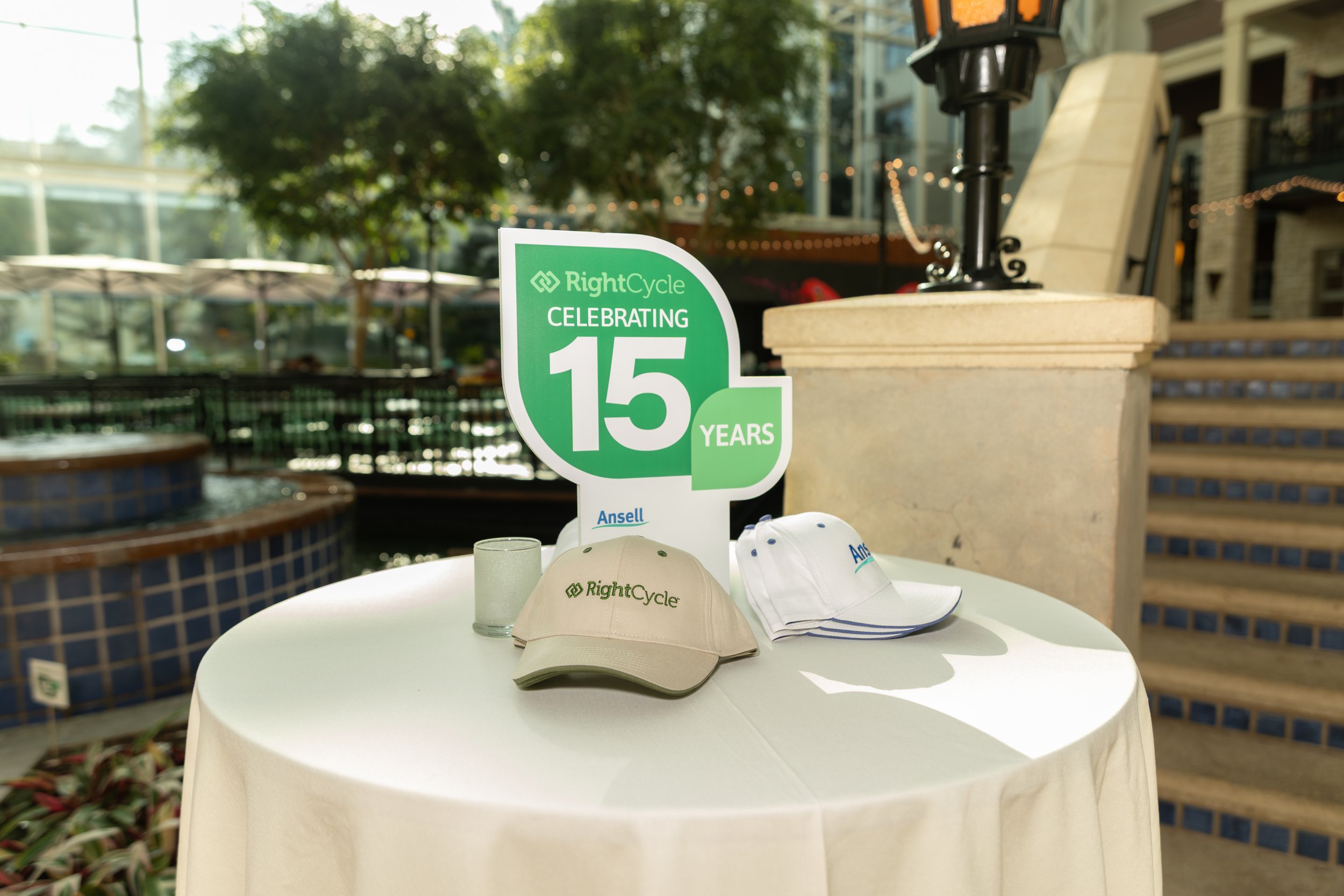 RightCycle 15th anniversary sign with branded hats and glass on a cocktail table at an outdoor venue