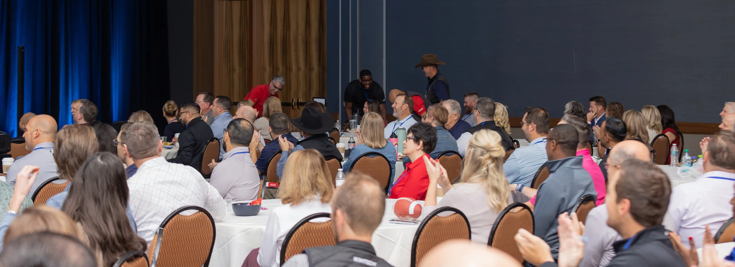 Audience applauding at a conference banquet with round tables and a stage