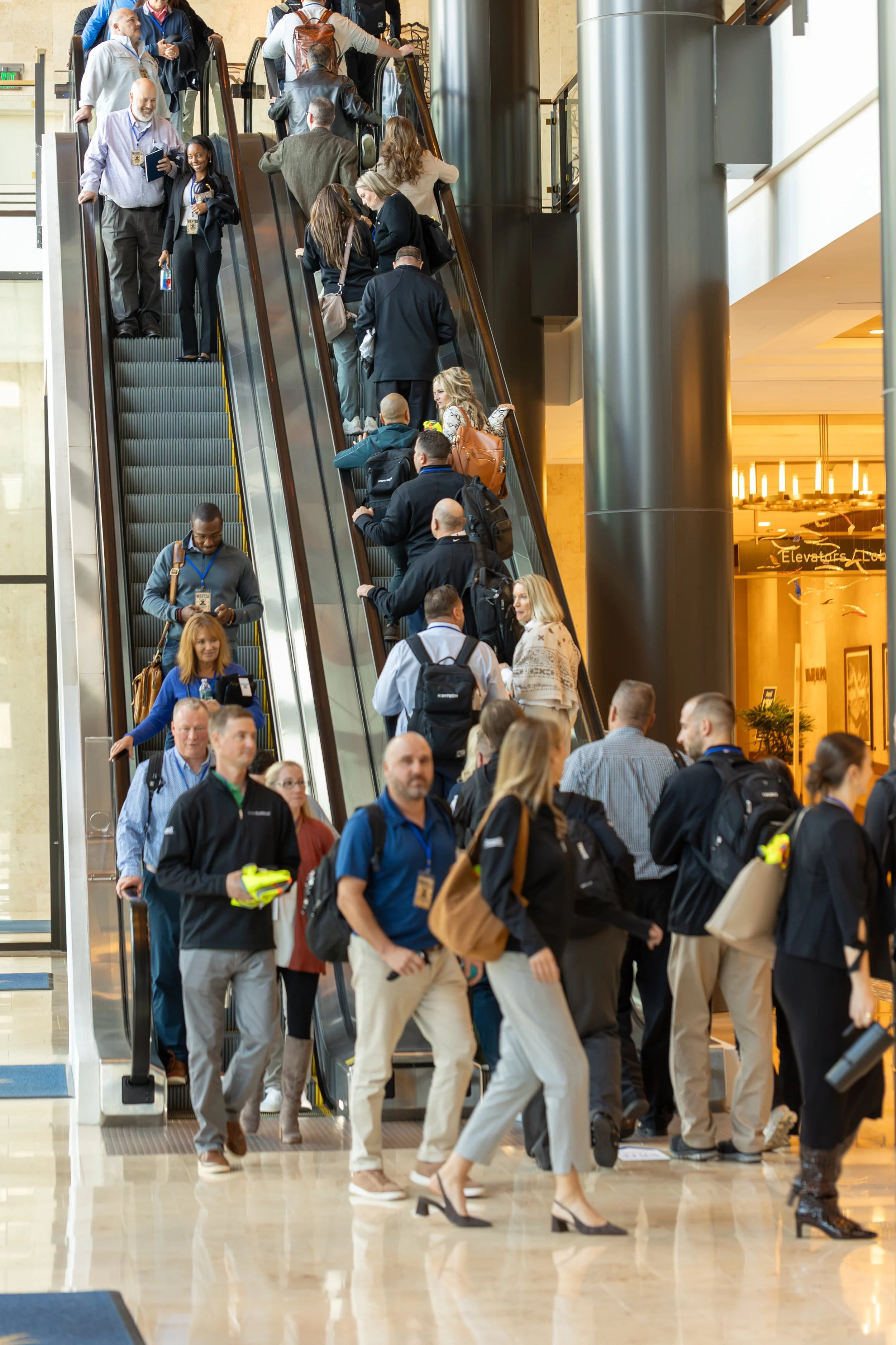 Crowd of convention attendees riding escalators in a hotel lobby
