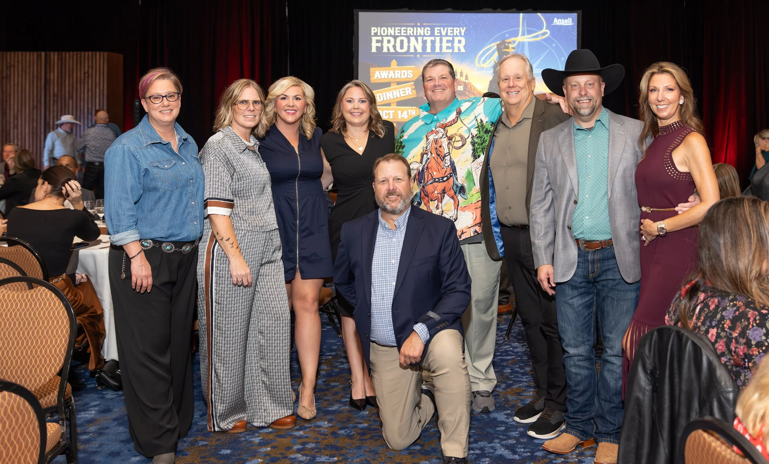 Group photo at an awards dinner with nine adults posing in front of a “Pioneering Every Frontier” event backdrop.