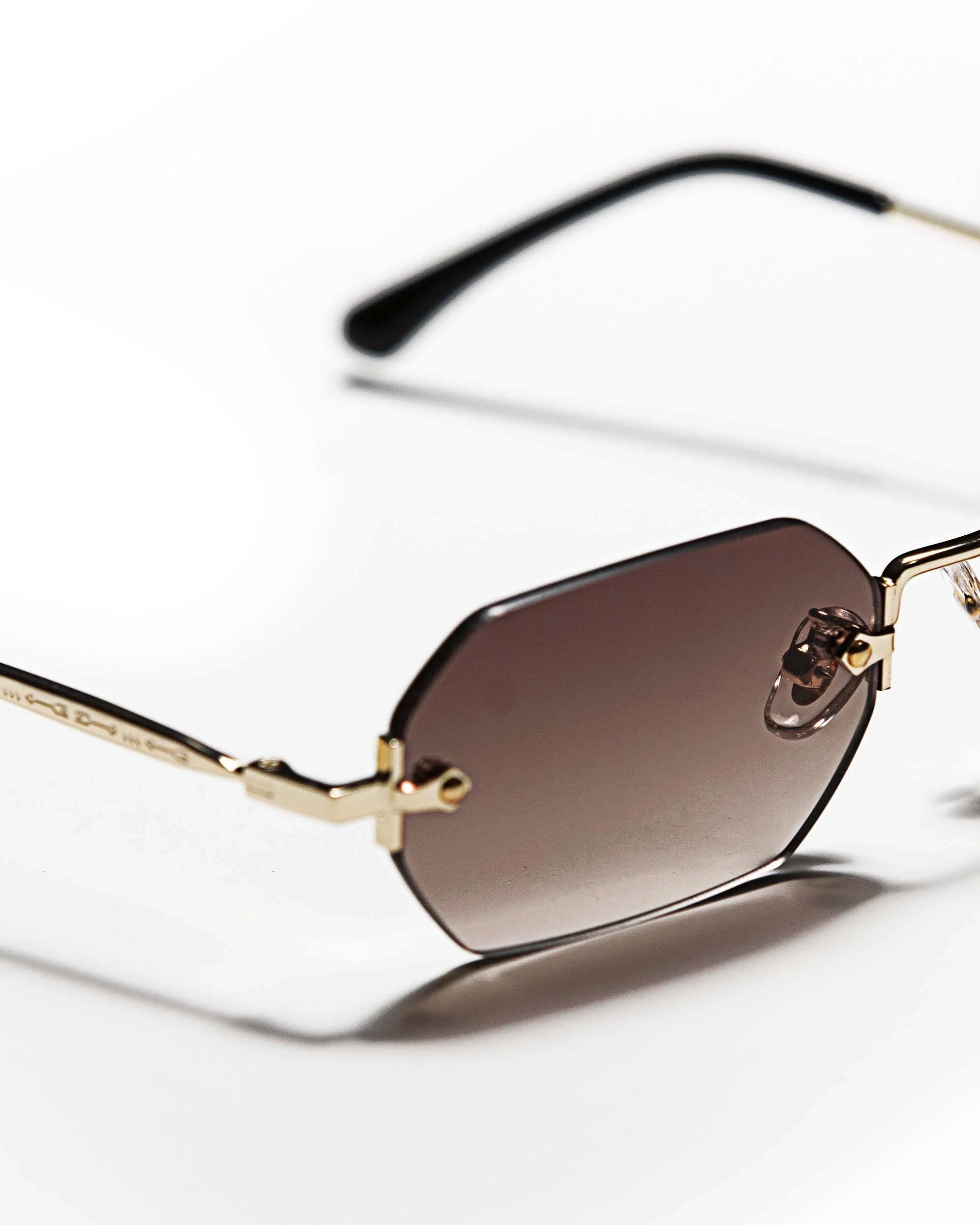 A pair of sunglasses with gold-colored metal frames and dark tinted lenses placed on a white surface.