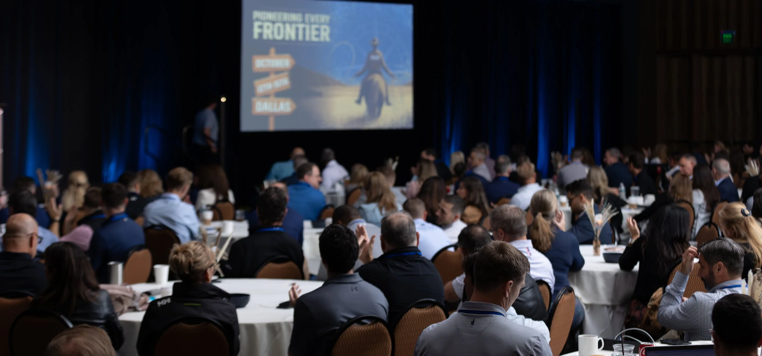 Audience seated at a conference presentation with a projected "Frontier" event graphic on stage