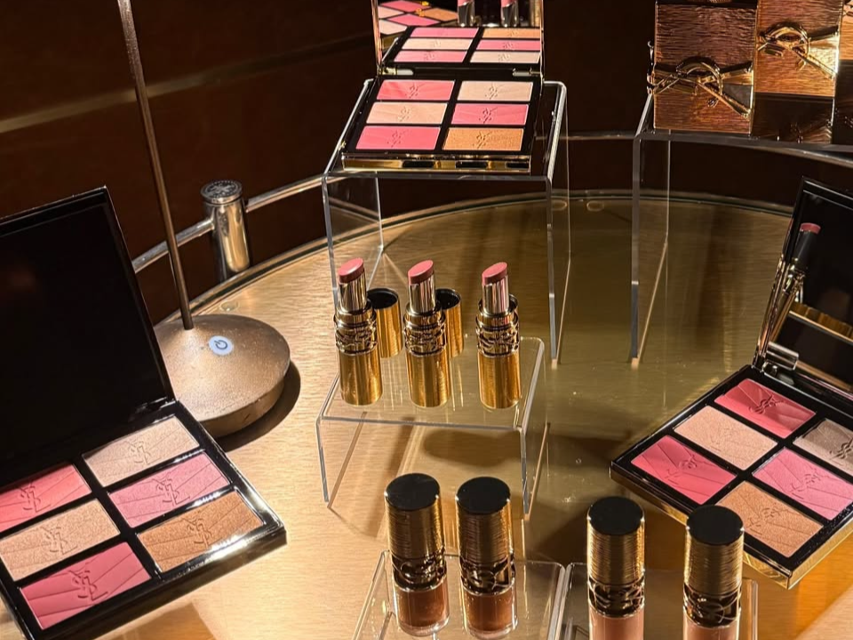 Makeup display with eyeshadow palettes, lipstick tubes, and foundation bottles on a wooden table.