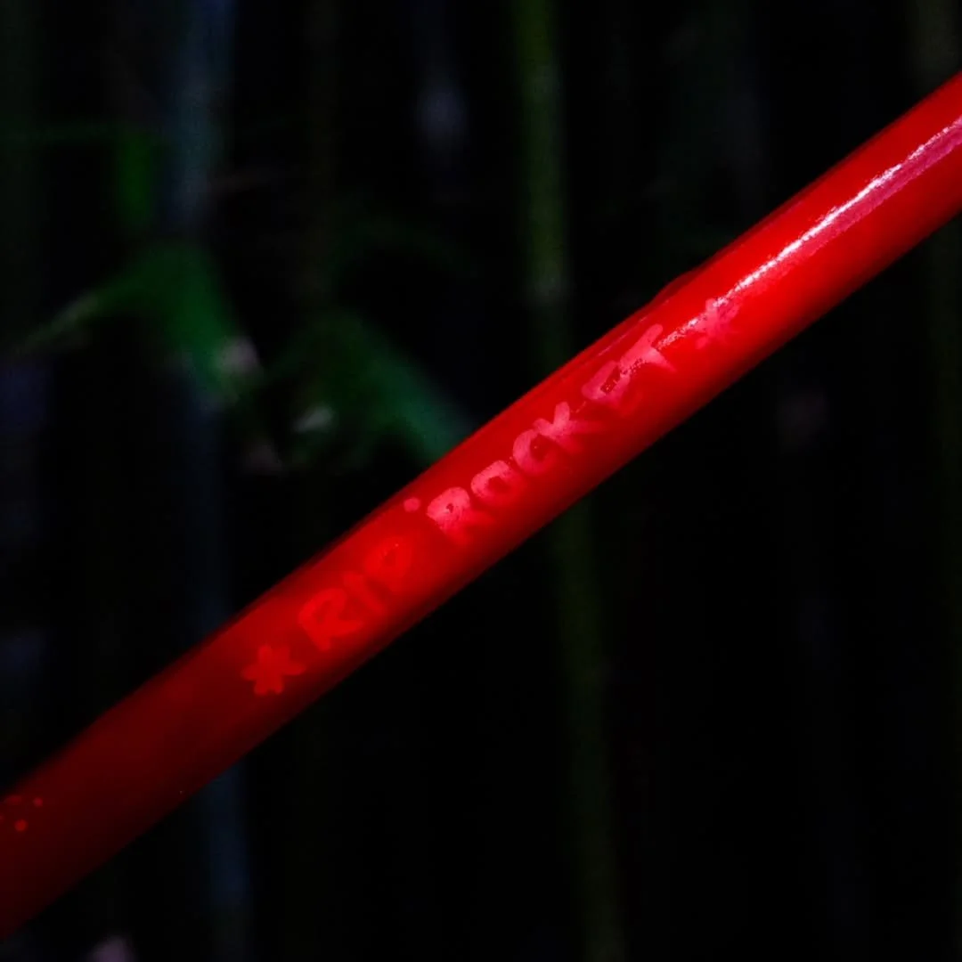 Close-up of a red plastic stake with embossed text, surrounded by dark greenery.
