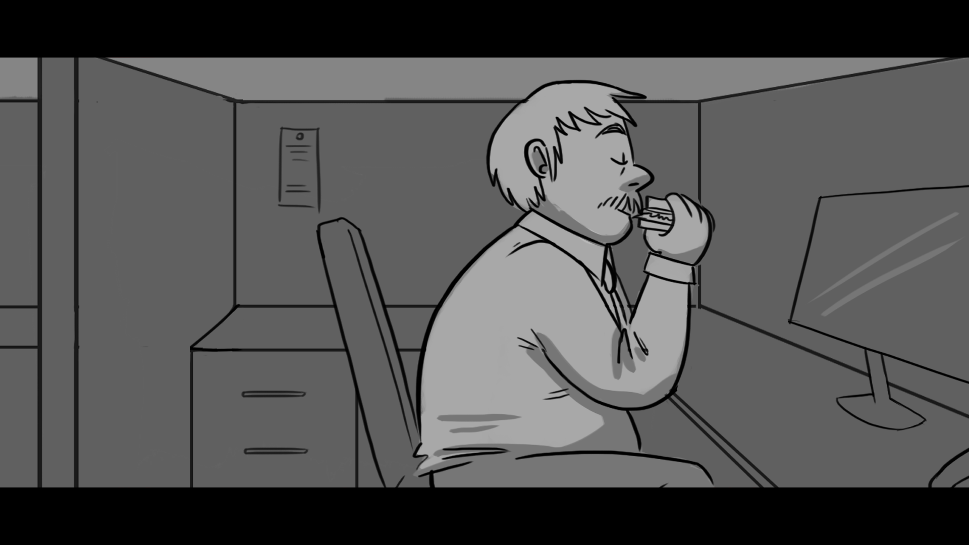 A man with a beard and short hair sitting at a desk in an office, eating a sandwich while looking at a computer monitor.