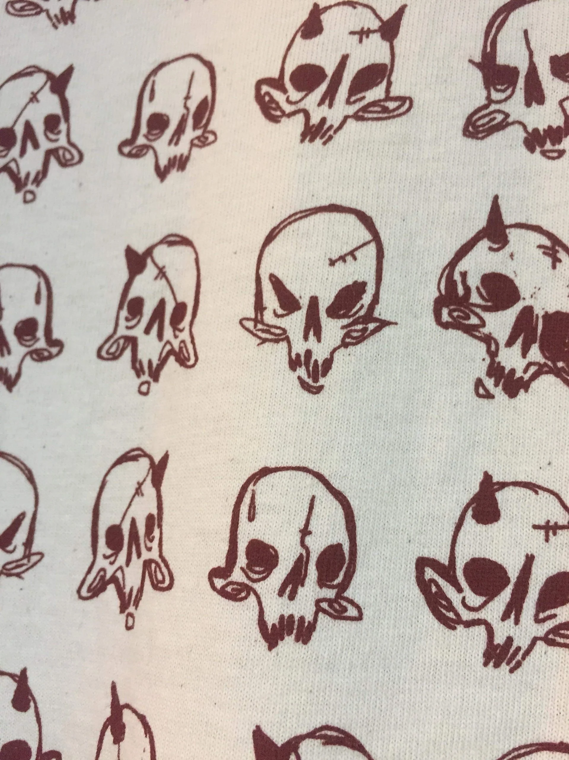 Pattern of hand-drawn skulls in black ink on white fabric.