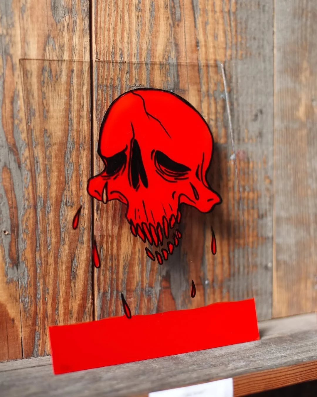 Red skull sticker with black details and dripping blood on a wood surface.