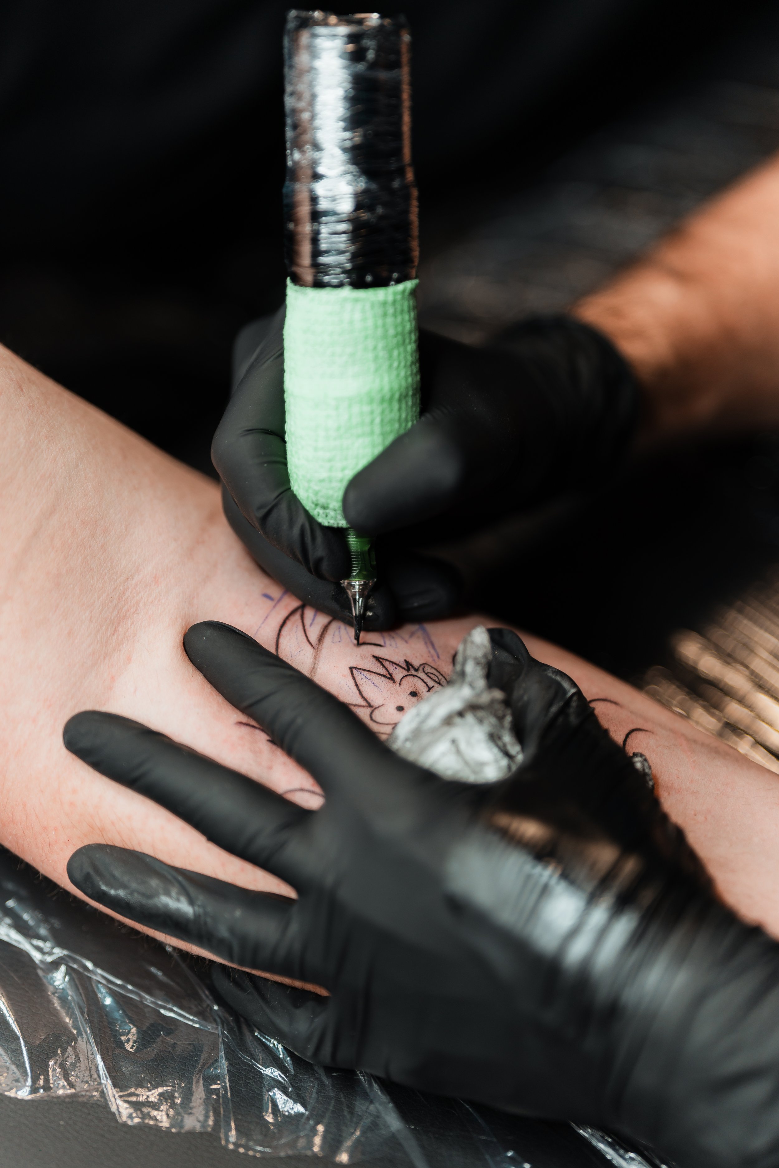 Person erhält ein Tattoo auf dem Arm; Tätowierer trägt schwarze Handschuhe.