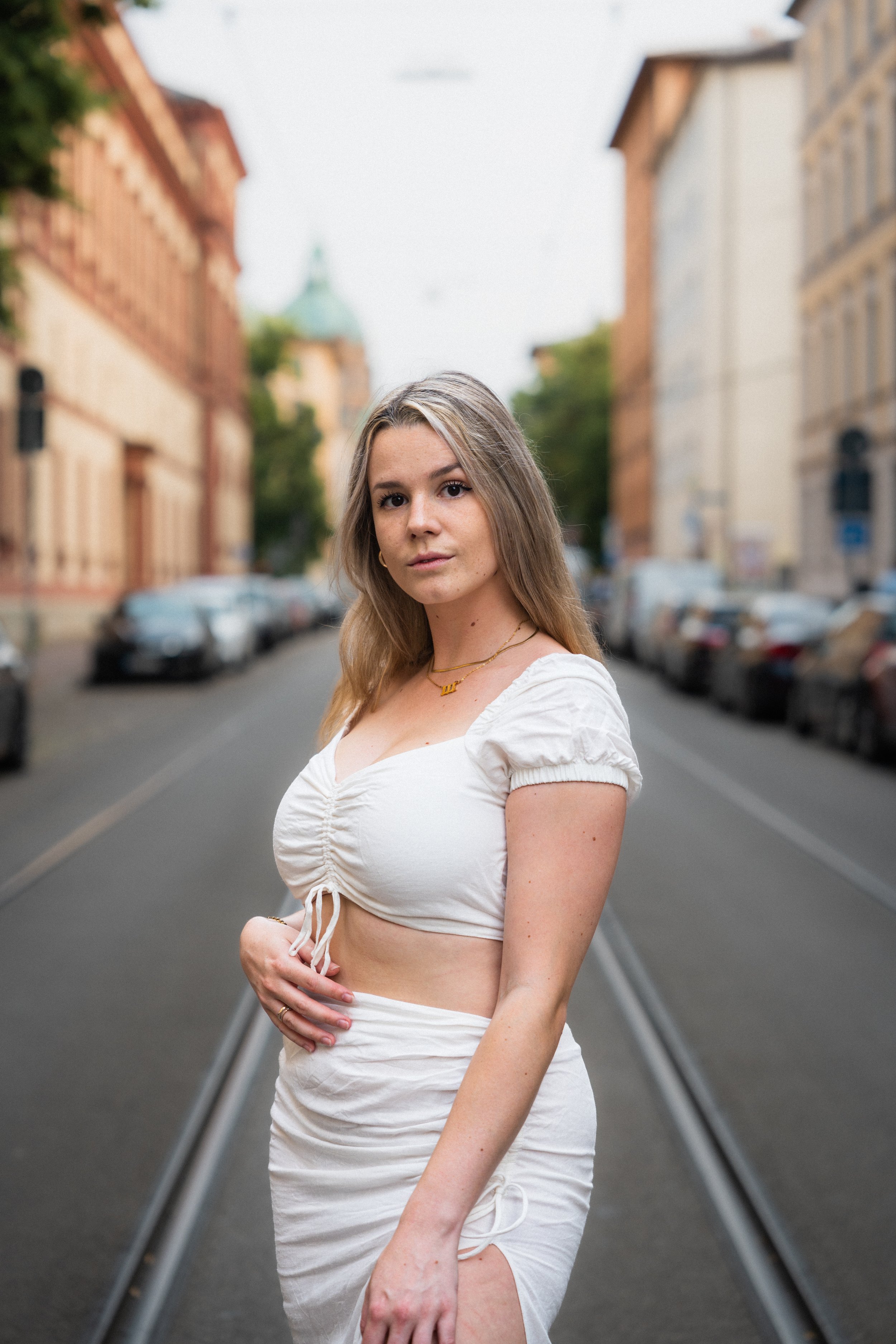 Frau in weißem Kleid steht auf einer städtischen Straße.