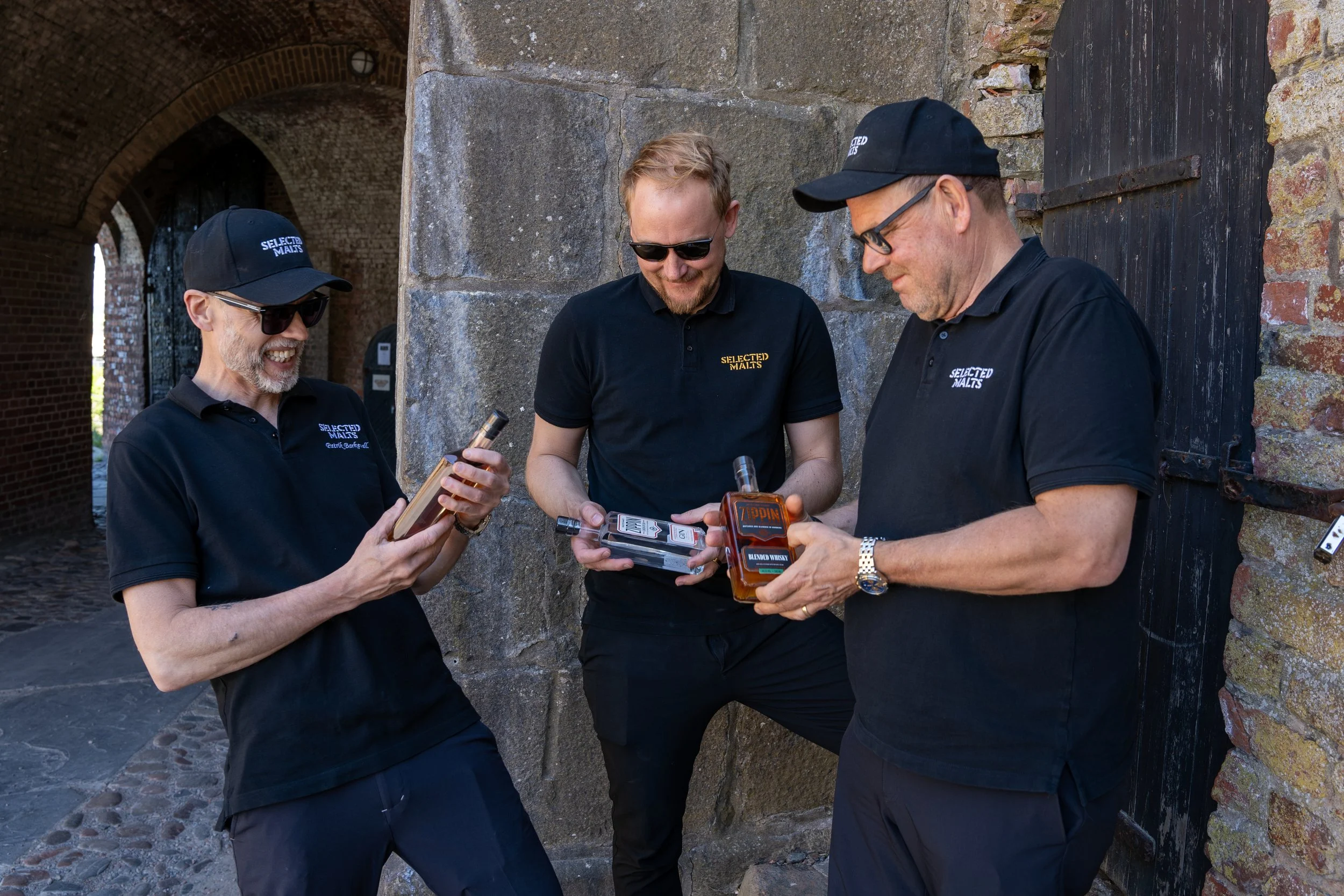 Three men dressed in black polo shirts and caps with the