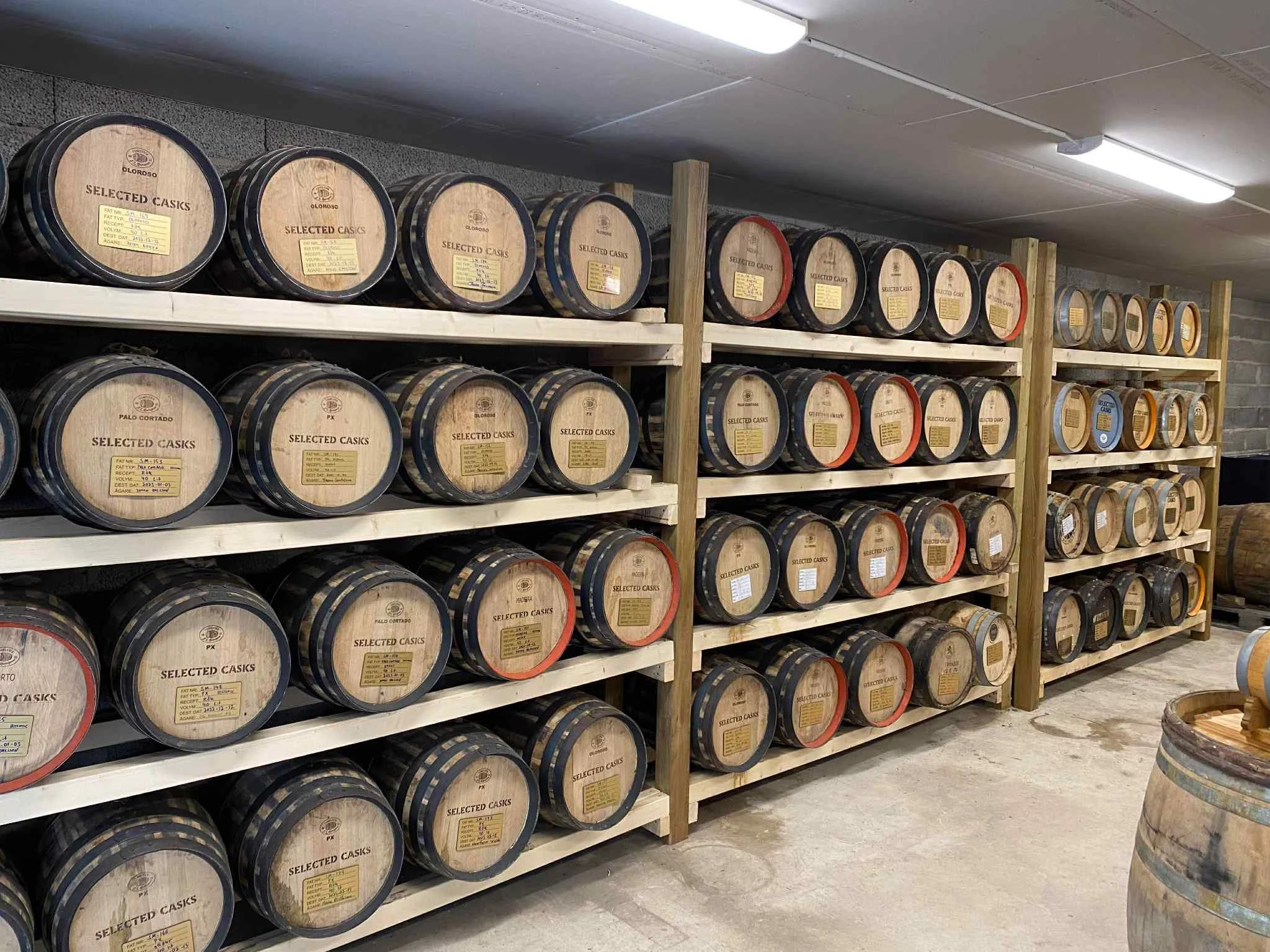 Shelves stocked with multiple wooden barrels of aged spirits or whiskey in a storage room.