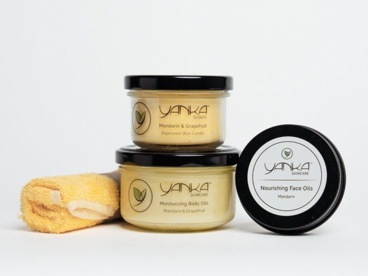 Yanka Skincare products, including a candle, body oil, and face oil, arranged with a yellow facecloth on a white background.