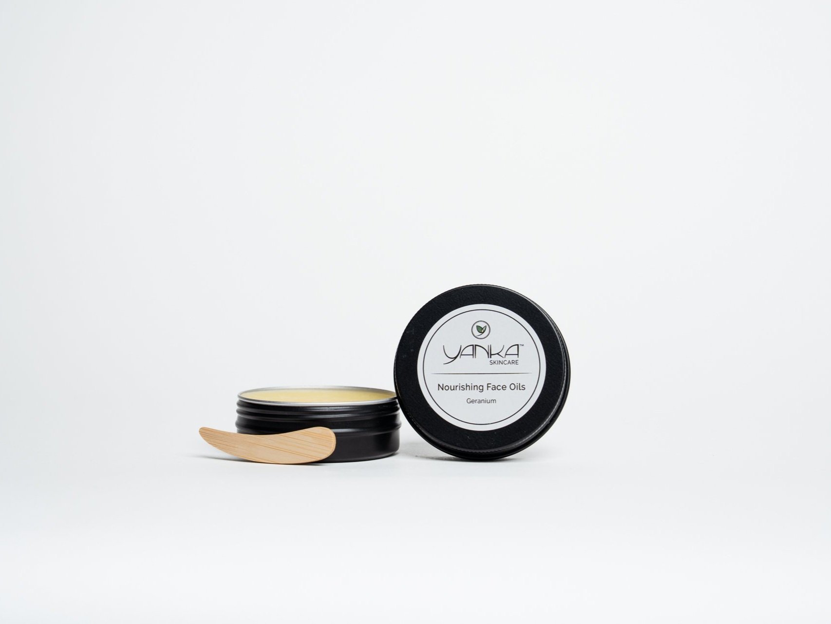 Yanka Skincare Nourishing Face Oils tin, open with balm inside and a wooden spatula, on a white background.