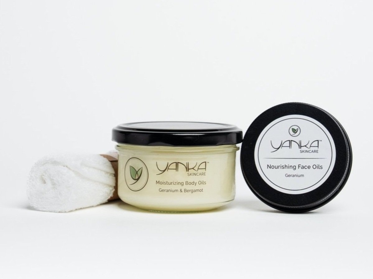 Yanka Skincare geranium & bergamot body oil and nourishing face oil, displayed with a neatly rolled white towel on a clean white background.