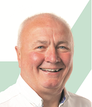 A smiling older man with a bald head and light complexion, wearing a white shirt.