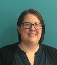 A woman with short dark hair and glasses smiling in front of a teal wall.