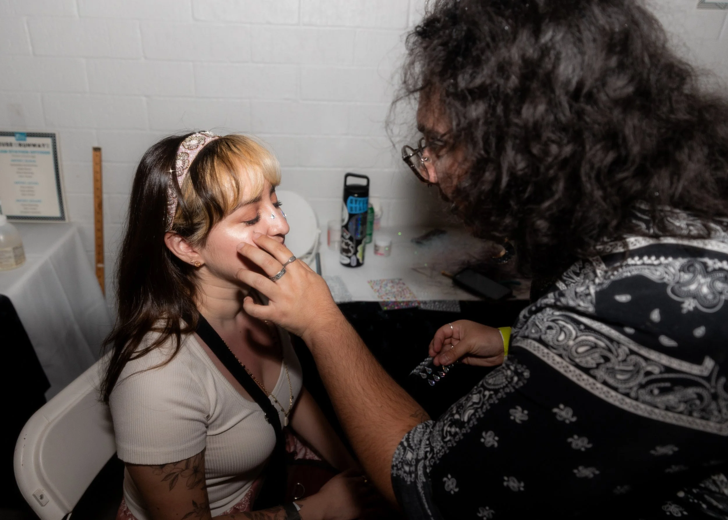 A makeup artist applies facial glitter to an audience member