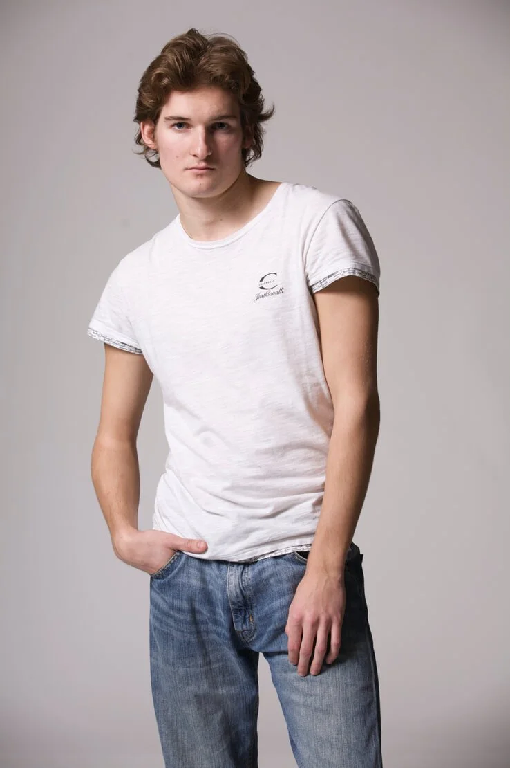 Jeune mannequin homme en t-shirt et jean, portrait studio sur fond gris