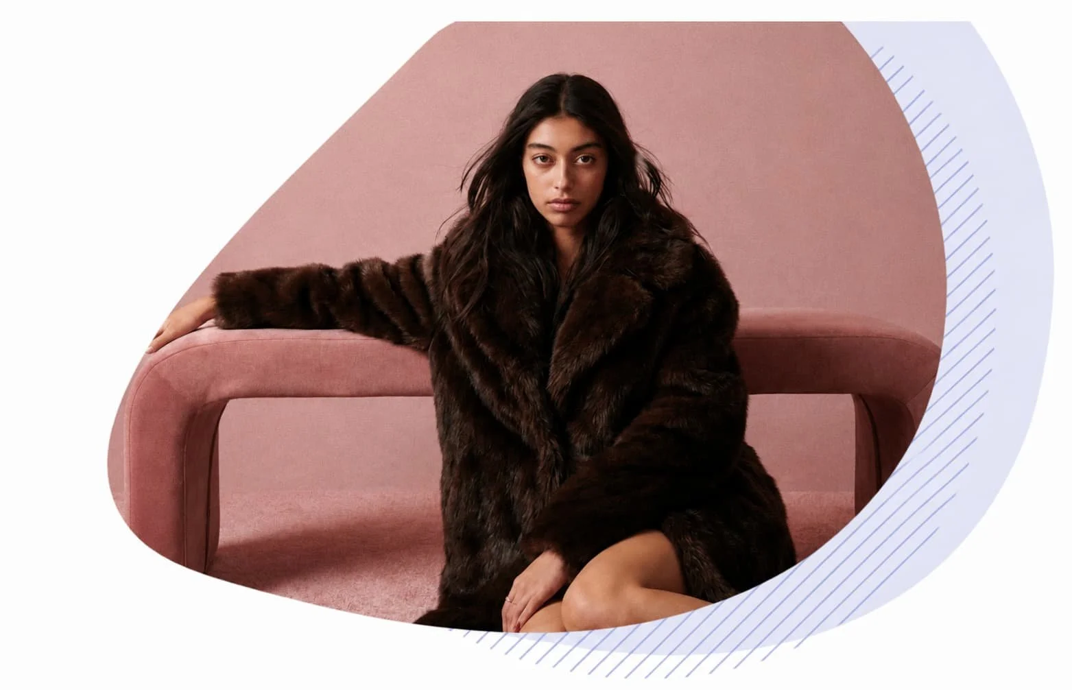 Jeune femme mannequin assise devant un banc rose dans un studio monochrome, portant un manteau en fausse fourrure sombre lors d'un shooting photo mode éditorial.