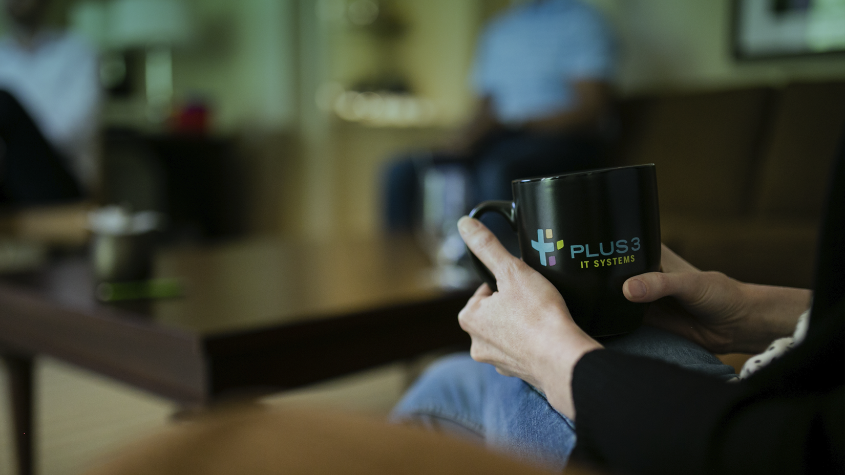 Person holding a black mug with a company logo in a cozy indoor setting.