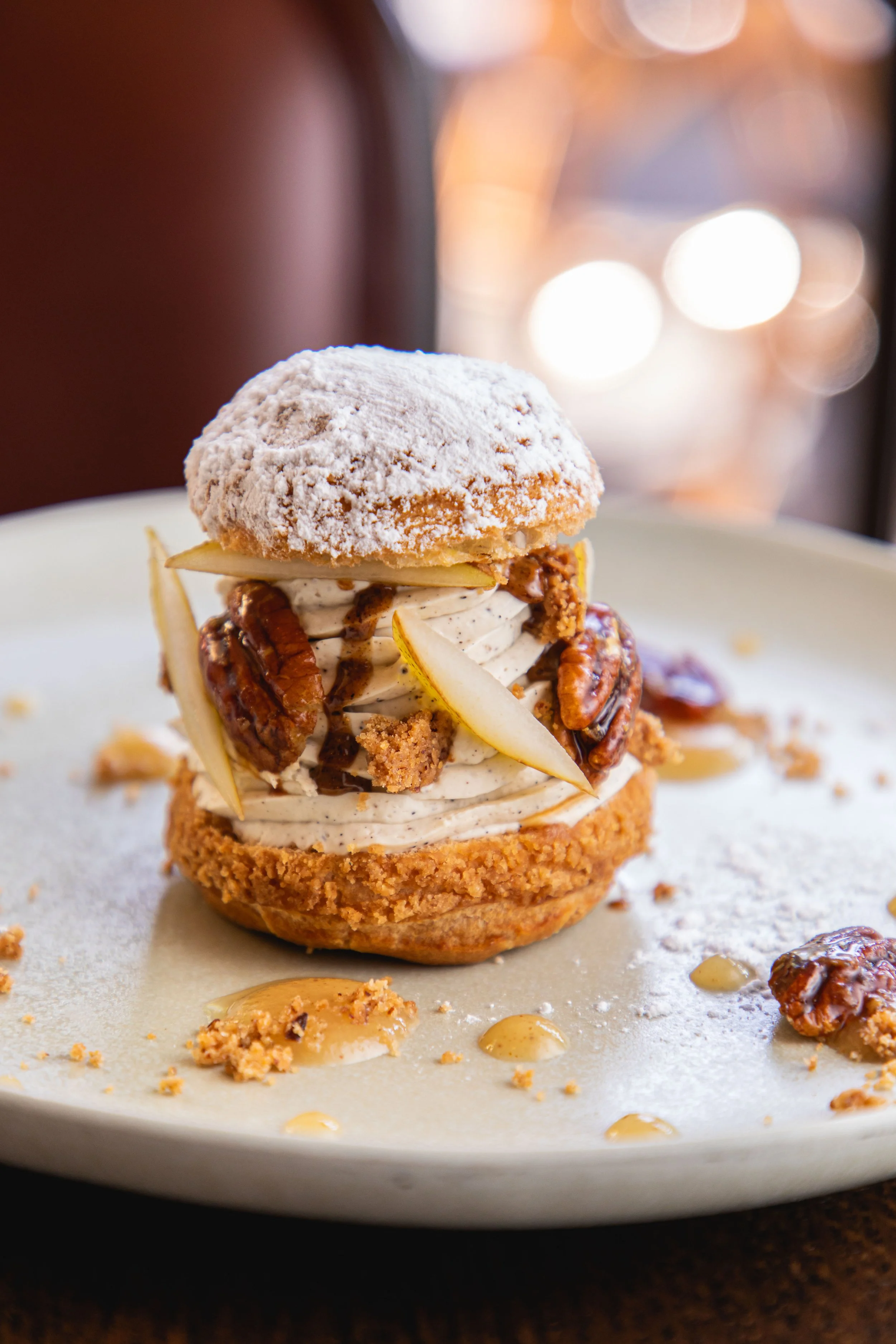 Un dessert avec une coque de gâteau, crème fouettée, poires, noix, sauce chocolat, toutes places sur une assiette blanche.