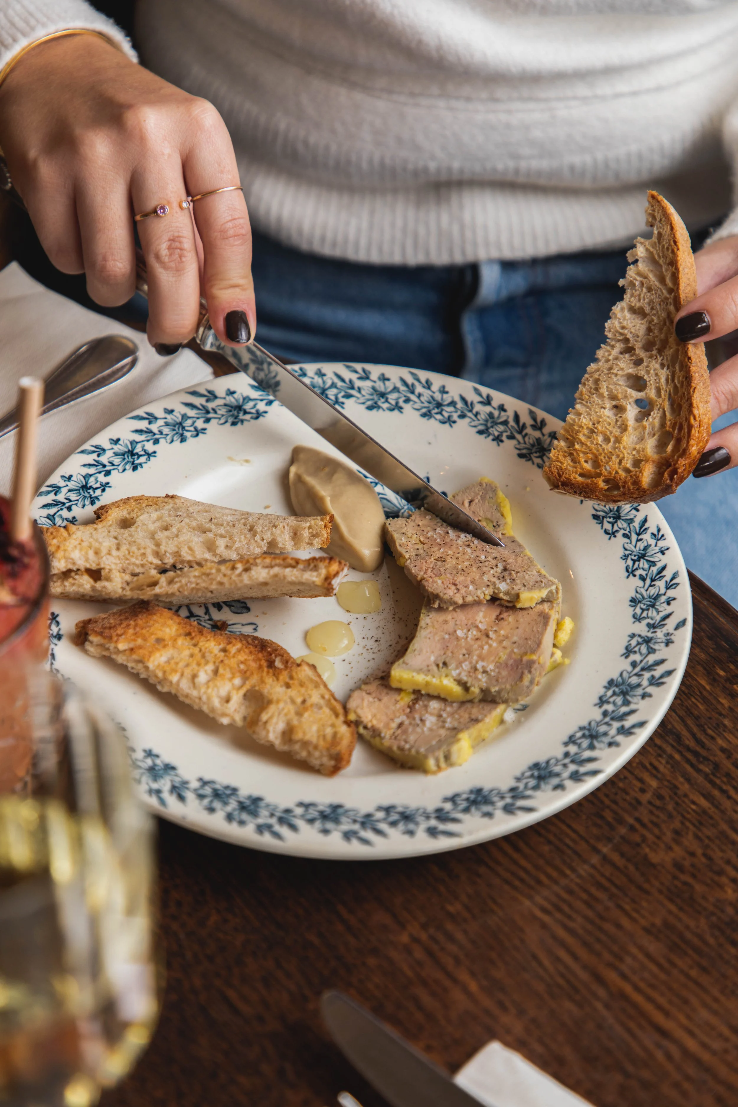Assiette avec terrine, rillettes, toast, et un peu de beurre, avec une personne en arrière-plan utilisant un couteau pour couper du pain.
