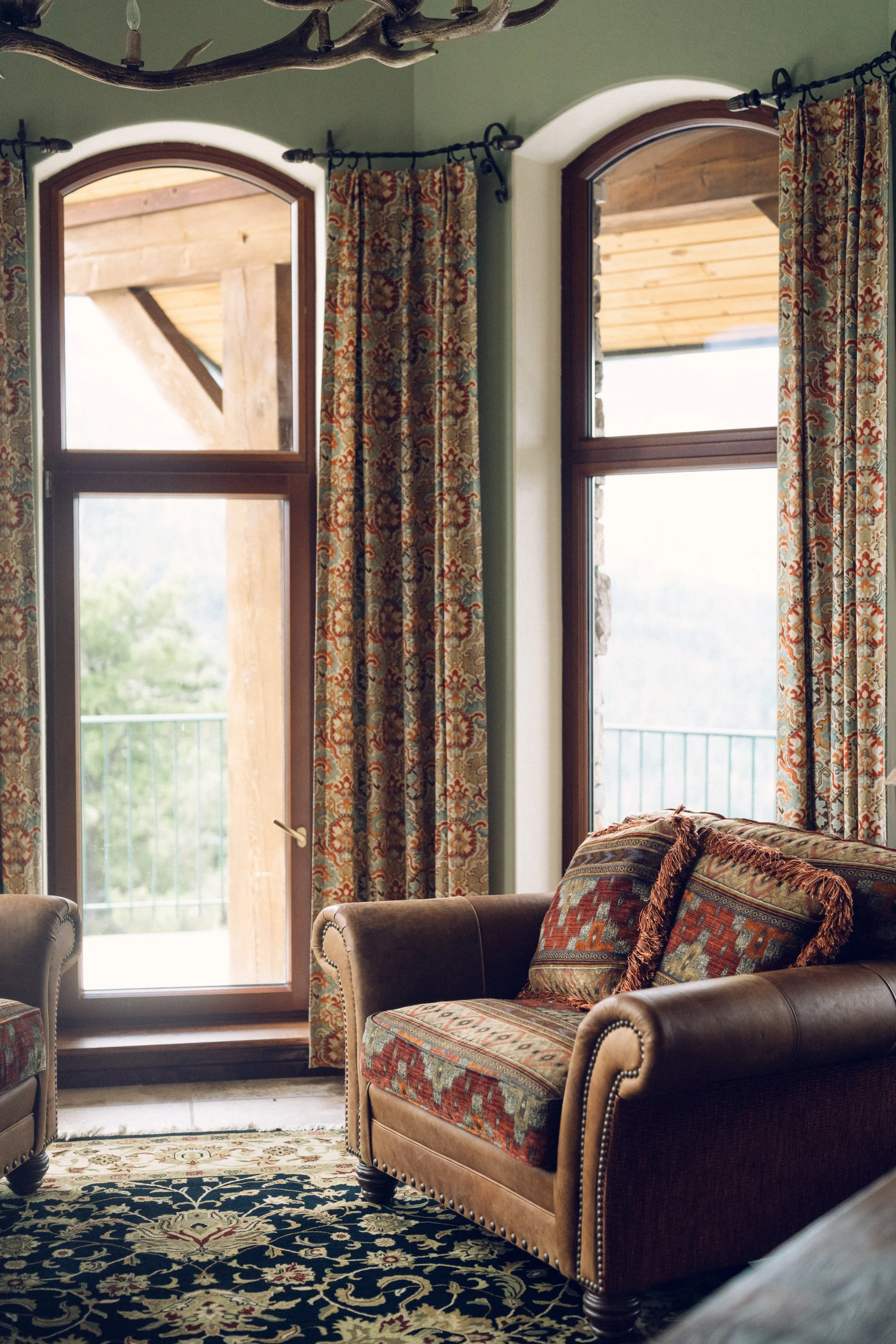 Living room with large windows, patterned curtains, and a sofa with decorative pillows.