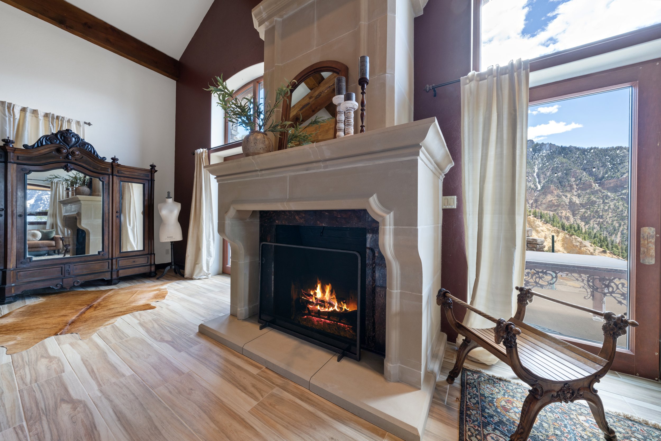 Living room with a fireplace, large window showing mountains, antique wooden furniture, a mannequin, and decorative items.