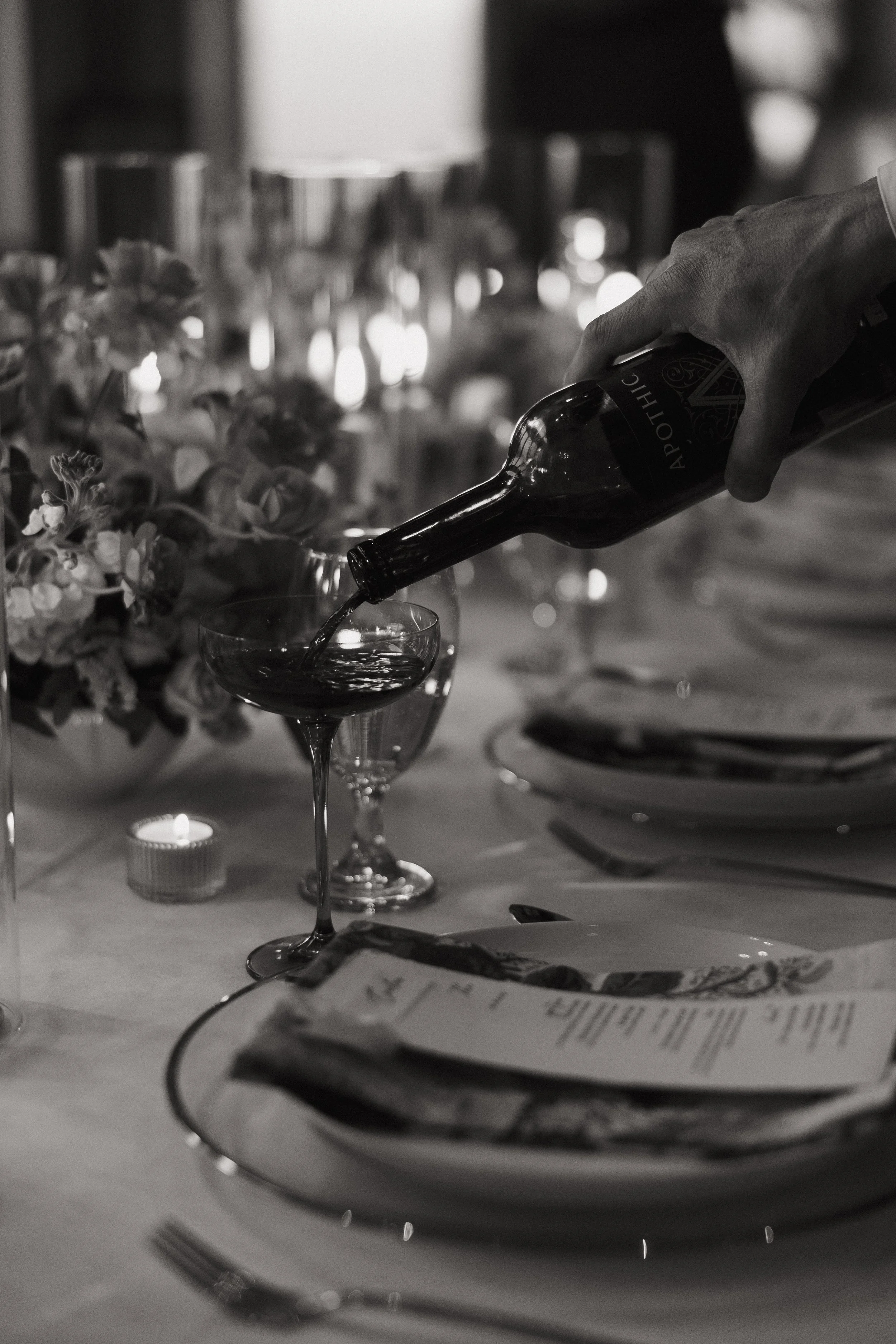 Pouring red wine into a glass at a formal dinner table with plates, cutlery, and floral centerpiece