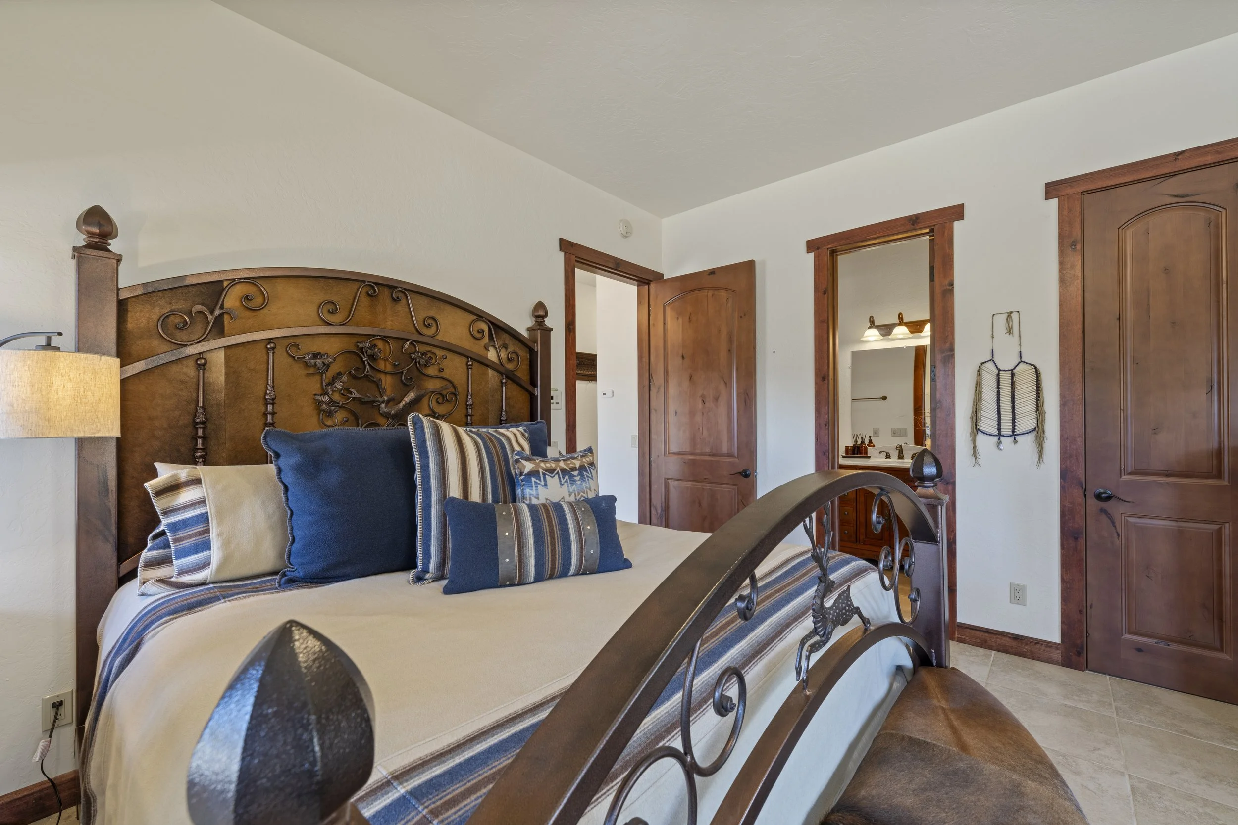 Bedroom with wooden bed frame, multiple blue and striped pillows, white walls, wooden trim, and an open door leading to a bathroom with a mirror and vanity.