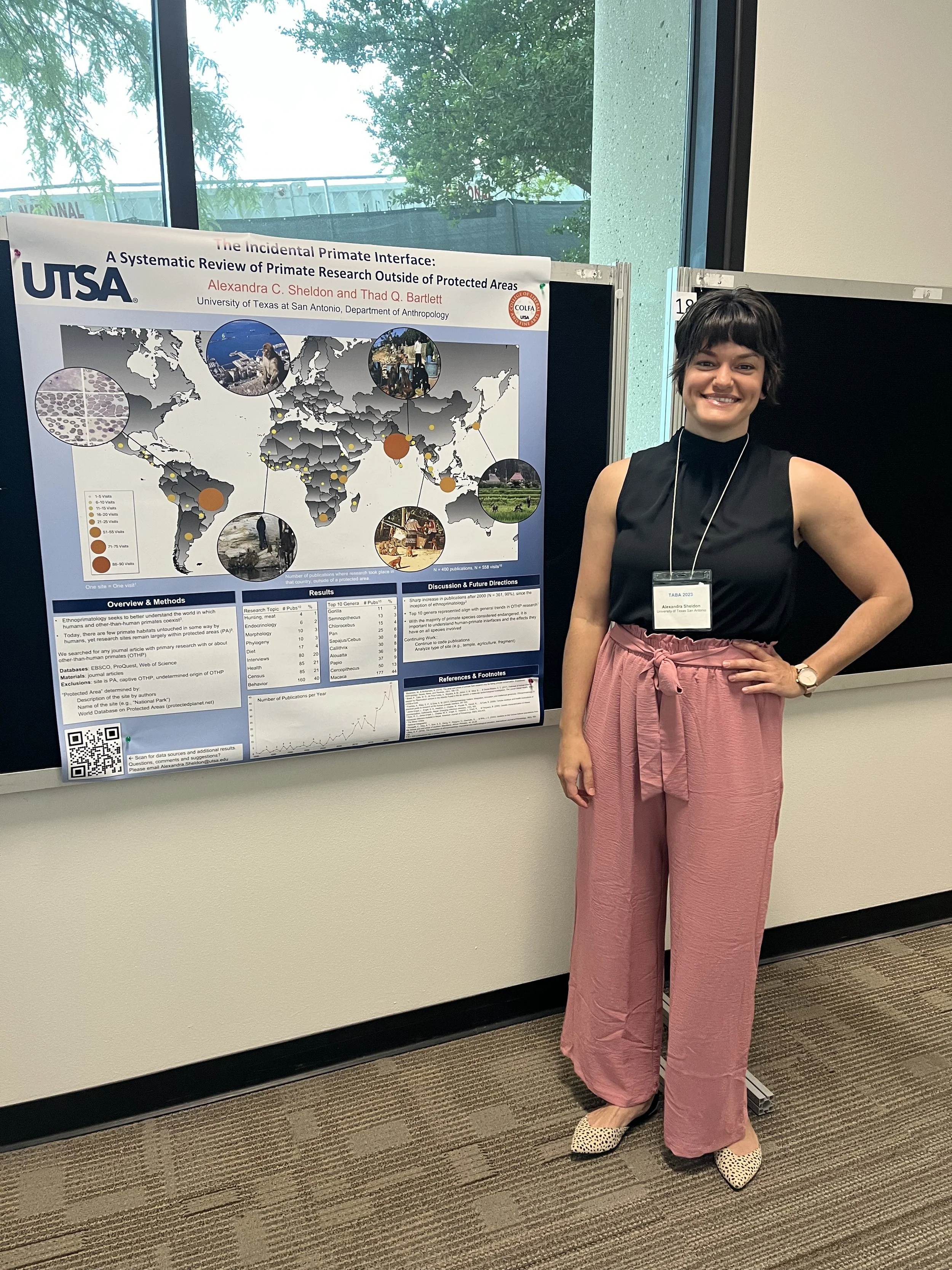 Woman wearing a black shirt and pink pants standing in front of a conference poster with map.