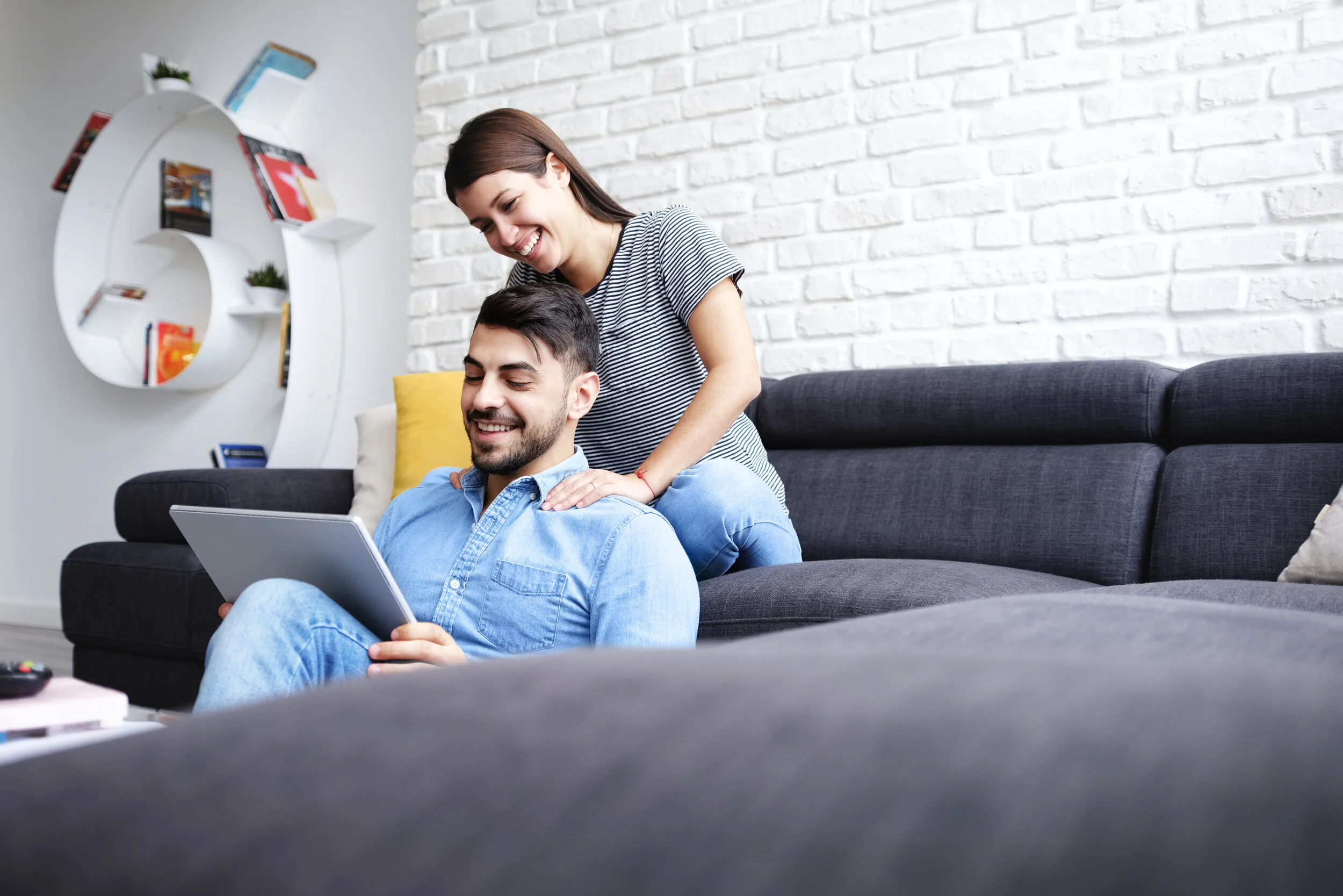 storyblocks-young-hispanic-couple-sitting-on-couch-at-home-using-a-tablet-pc-for-internet-and-social-media-the-girl-is-giving-a-massage-to-her-boyfriend-copy-space_SUEJGWiQX.jpg