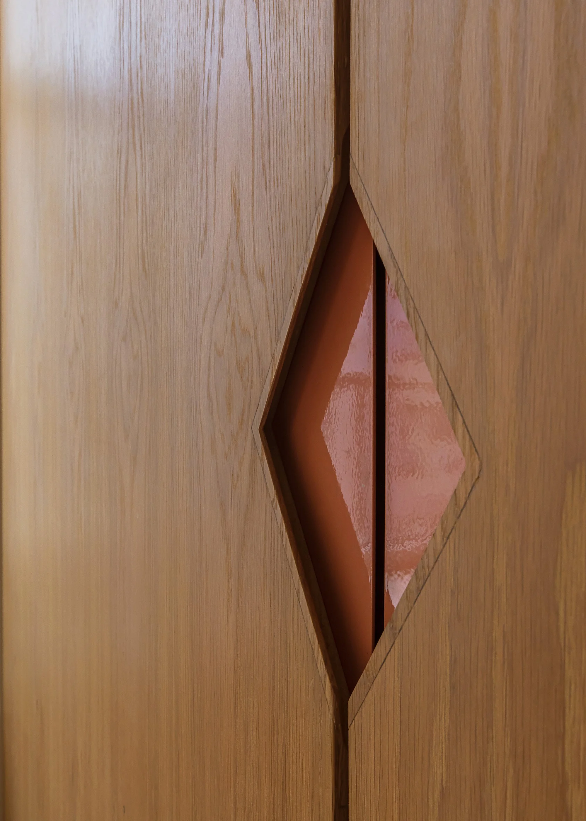 Custom integrated pull with triangular detail and pink powdercoated finish with white oak door