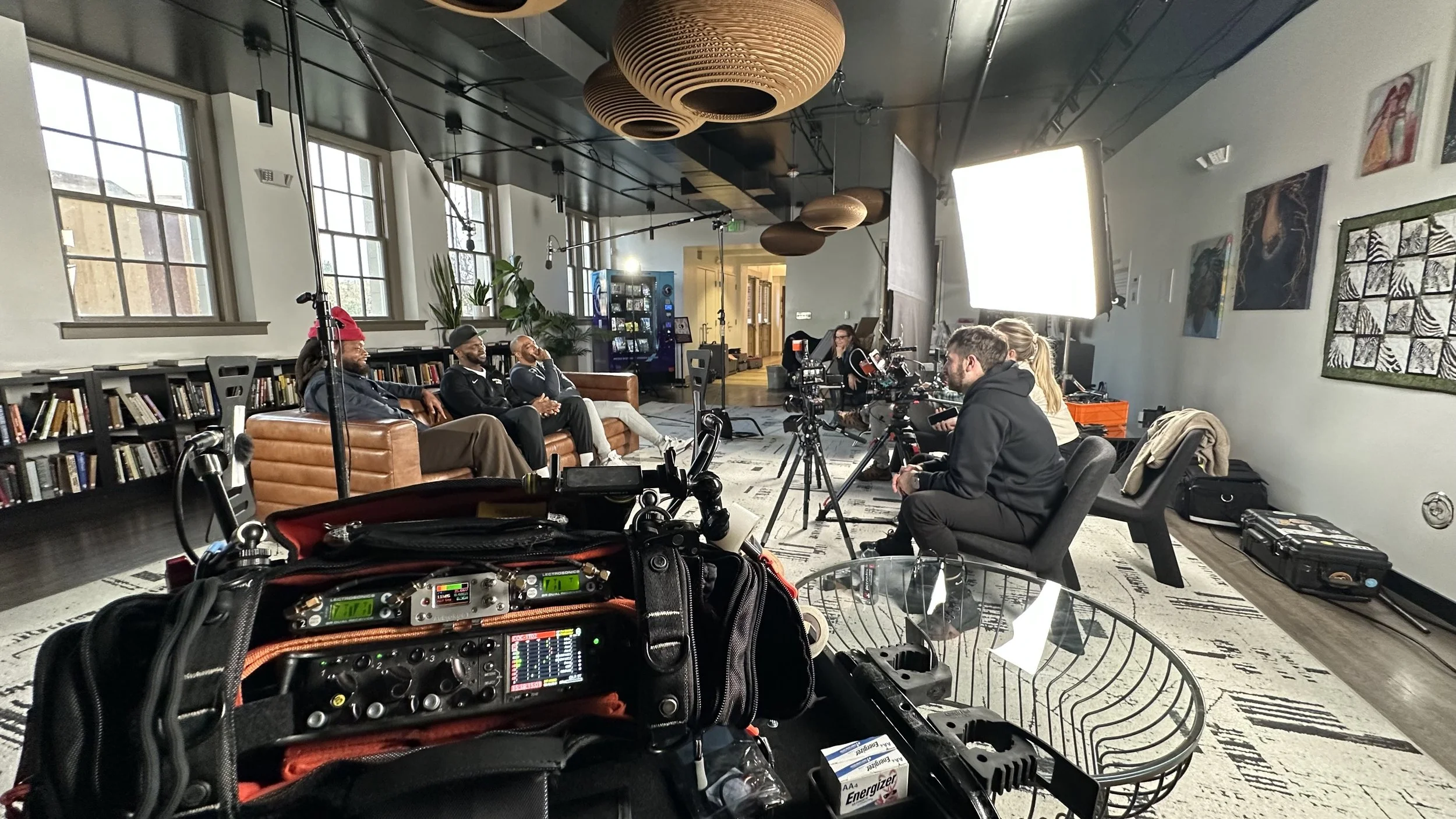 Interview production setup with camera, lighting, and crew in a community space.