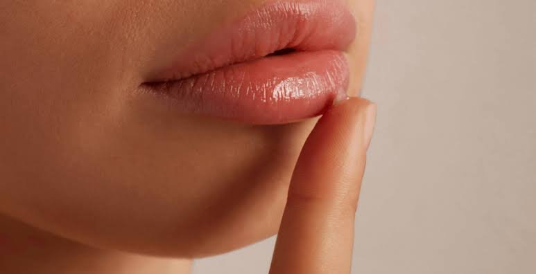 Close-up of a person's lips with finger pressed to lips in a 'shh' gesture.
