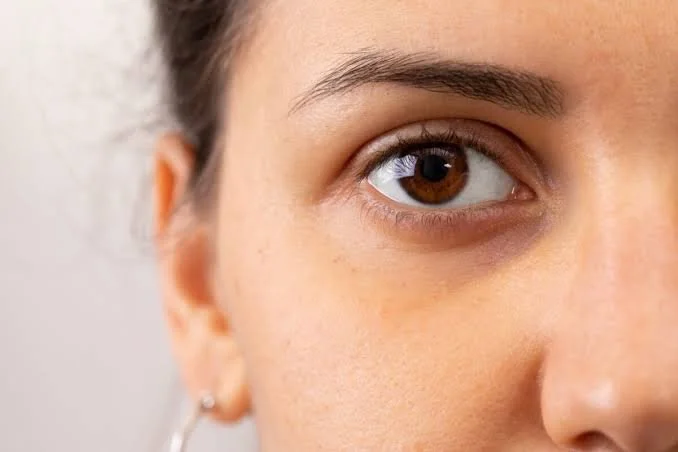 Close-up of a woman's face showing her brown eye, eyebrow, and part of her cheek with a small earring.