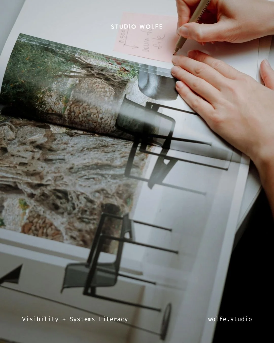 Hands writing on a small note above a printed editorial image, suggesting visual curation and creative decision-making.