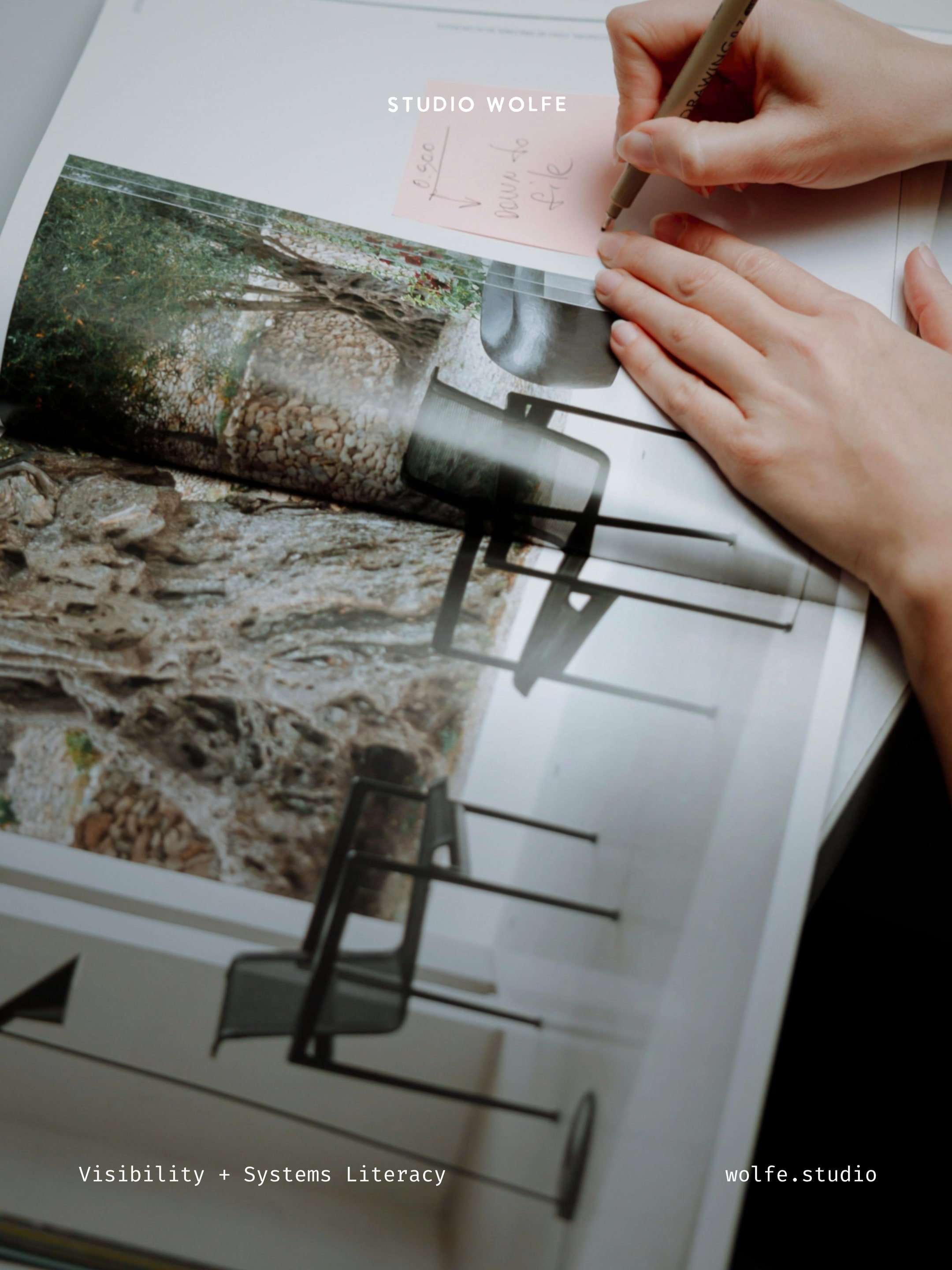 Hands writing on a small note above a printed editorial image, suggesting visual curation and creative decision-making.