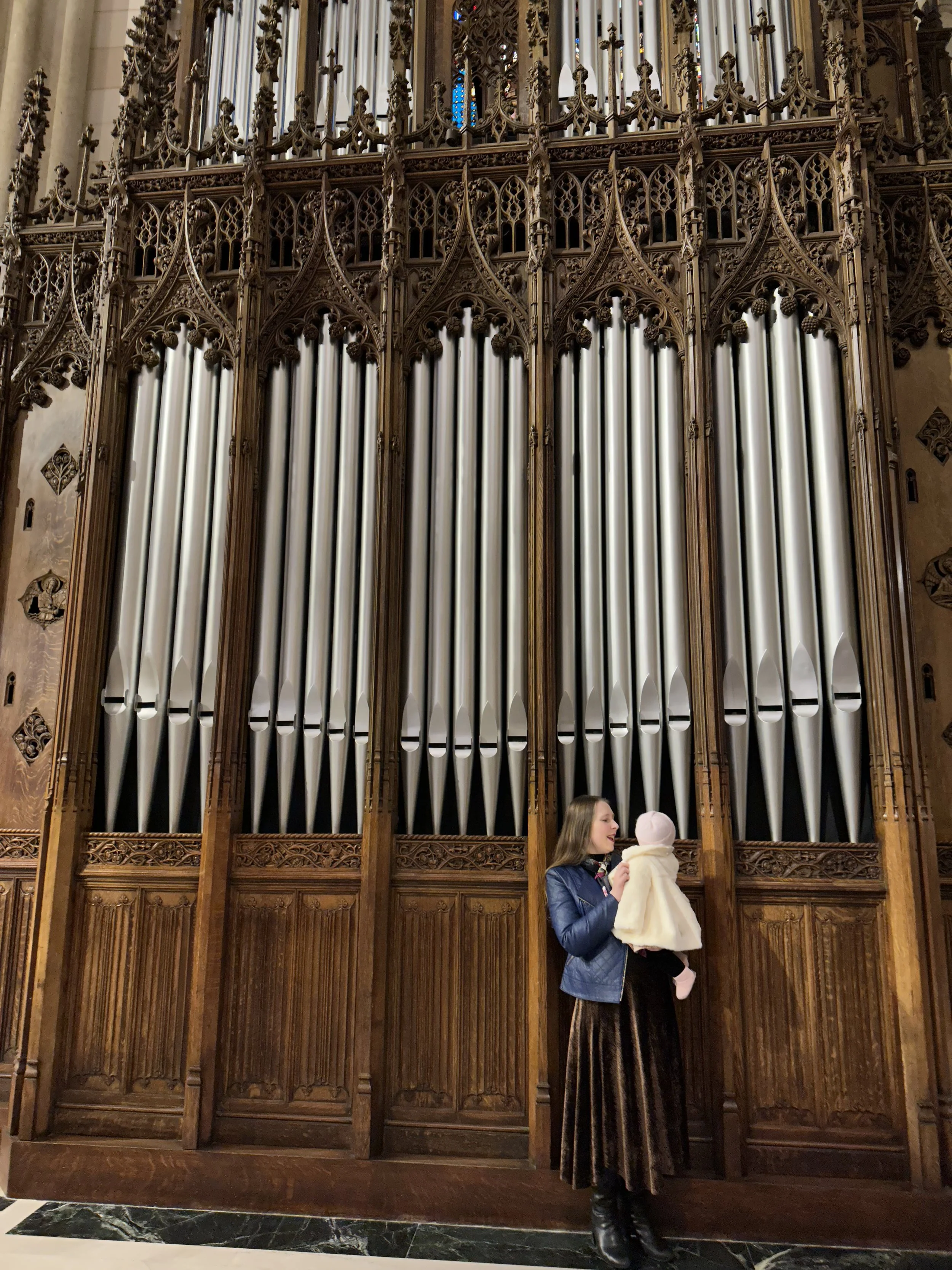 Sarah Jane Starcher Germani, organist and planner designer holds her infant daughter near the facade of the pipe organ of St.Patrick's Cathedral, Manhattan, NYC