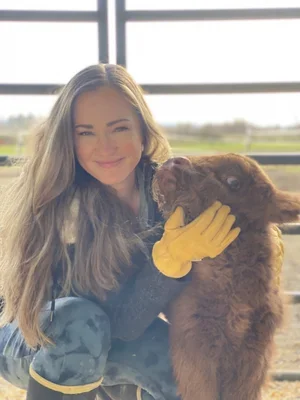 Smiling woman holding a highland cow wearing a yellow gloves