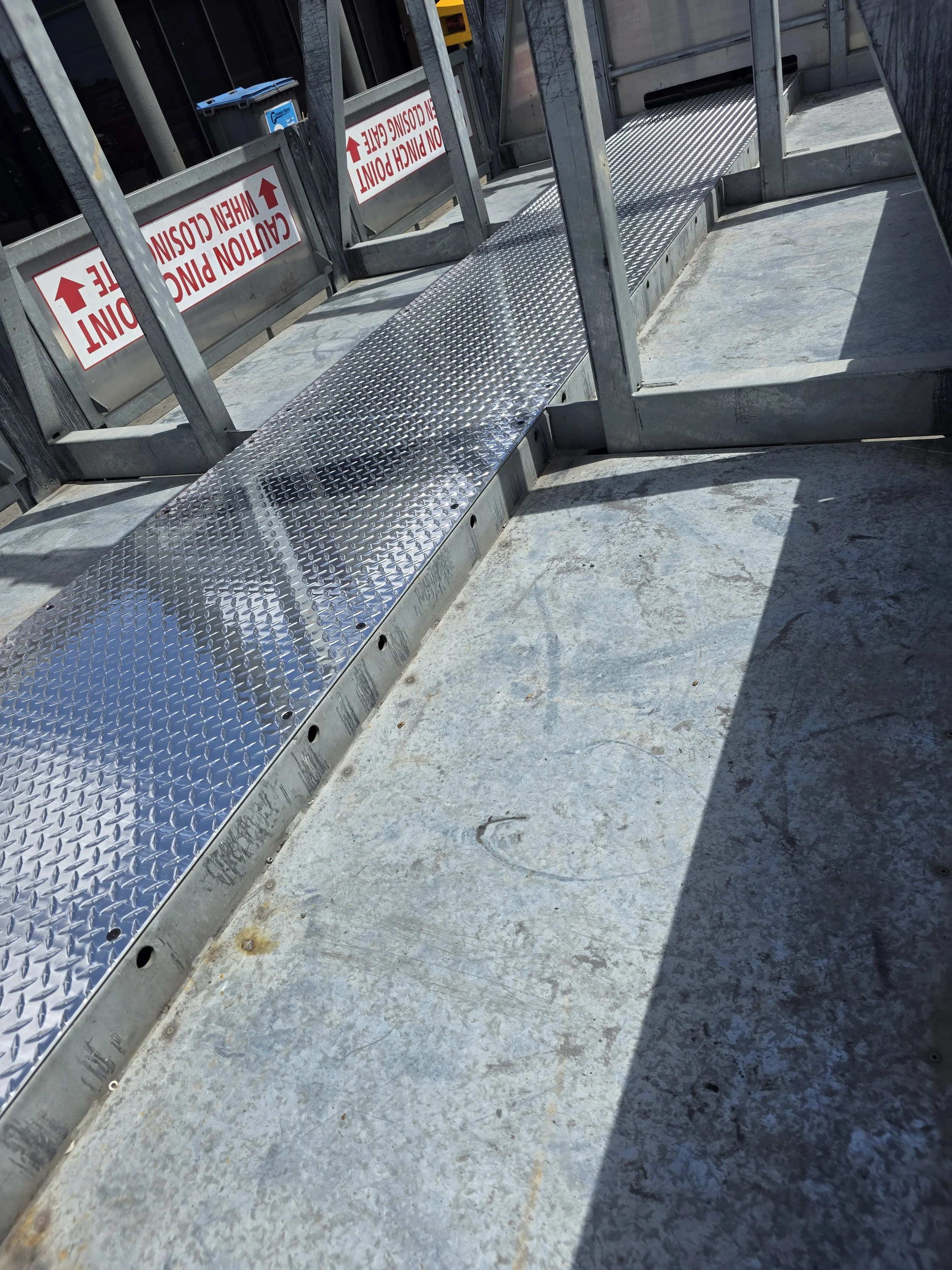 Metal scaffolding with warning signs, a textured metal walkway, and concrete ground with shadows.