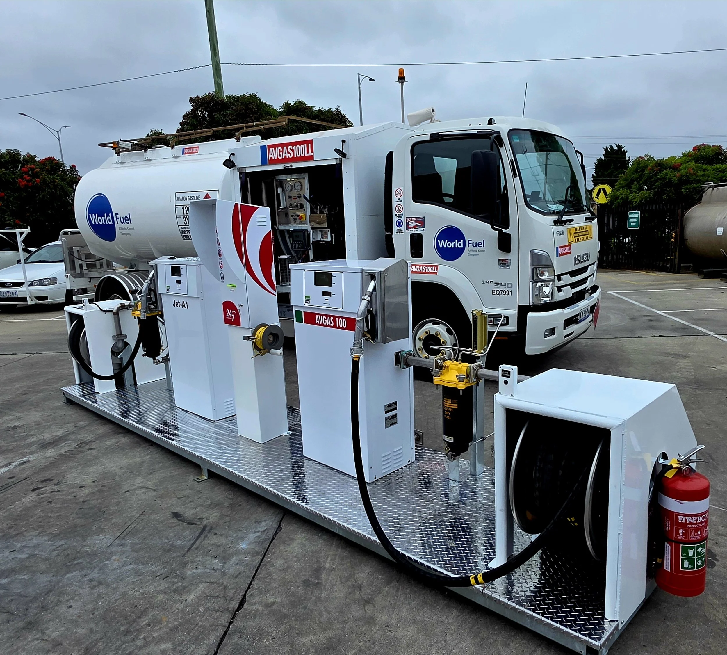 A fuel tanker truck with World Fuel branding at a fueling station, surrounded by other vehicles and equipment.