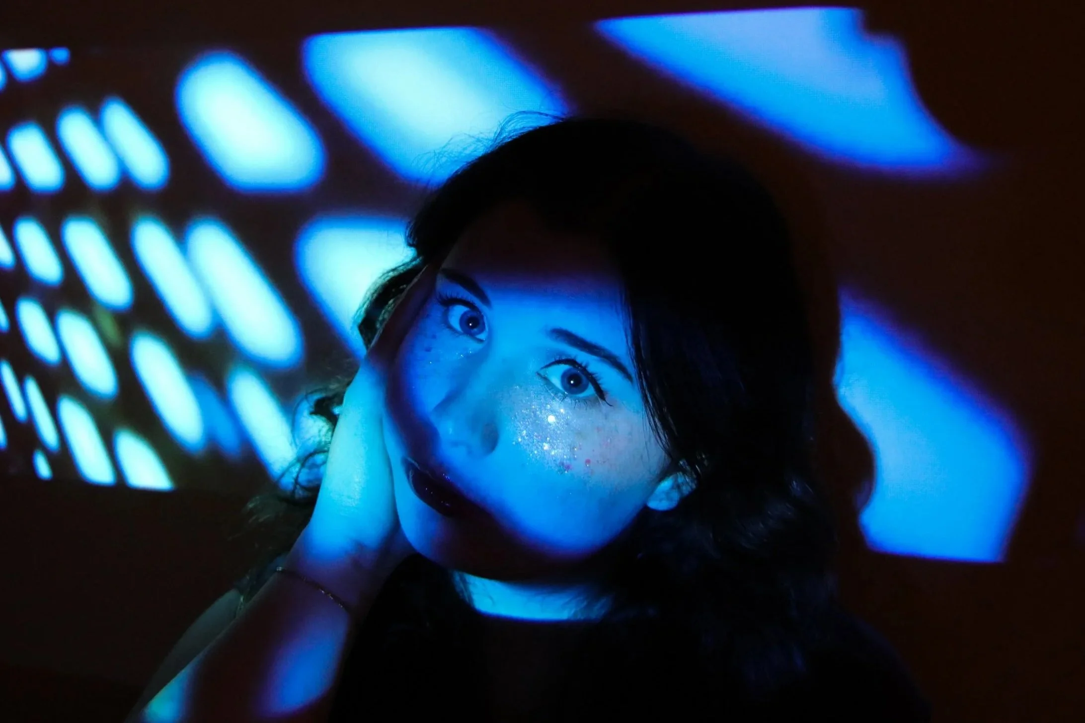 Claire Kantz press photo, looking right at the camera in blue projector light
