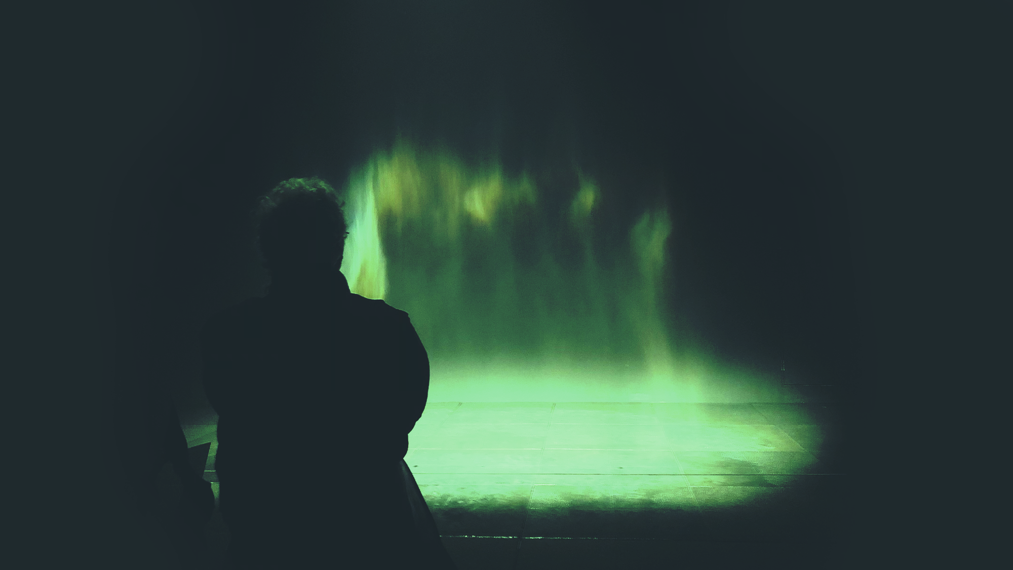 Silhouette of a person observing green Aurora Borealis inside a dark room.